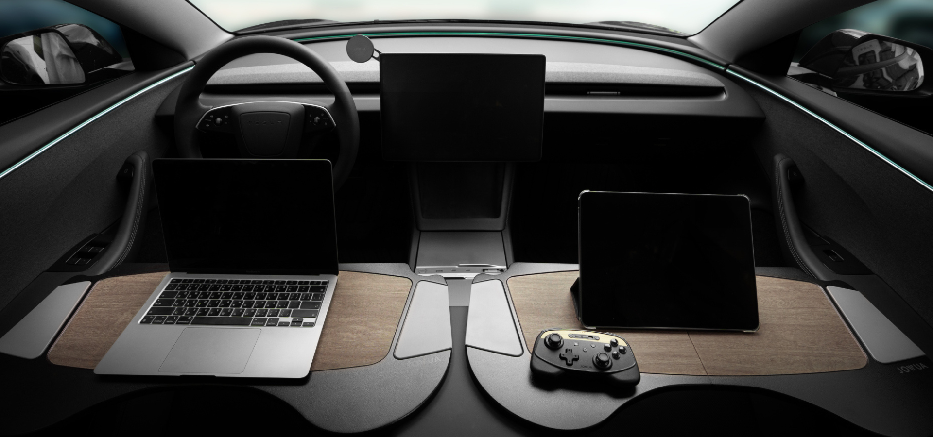 Futuristic car interior with two screens on the dashboard, a laptop on the passenger side, and a gaming controller on a wooden surface. The design is sleek and modern.