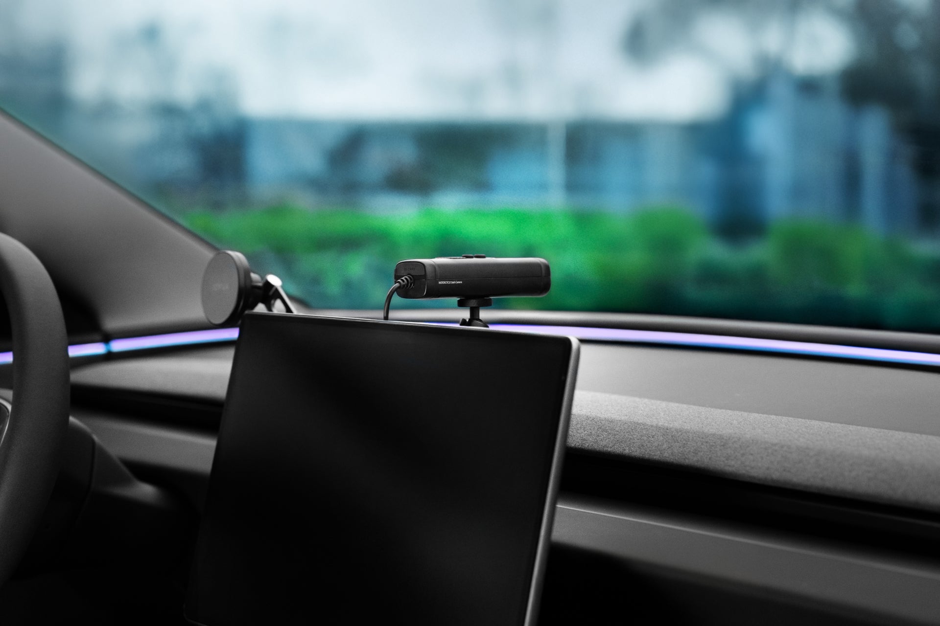 The JOWUA 360° Multi Function Mount camera is elegantly positioned on a car dashboard, offering versatile photography angles with its adjustable ball head. The interior features a large screen, accented by visible greenery through the windshield, showcasing its modern design.