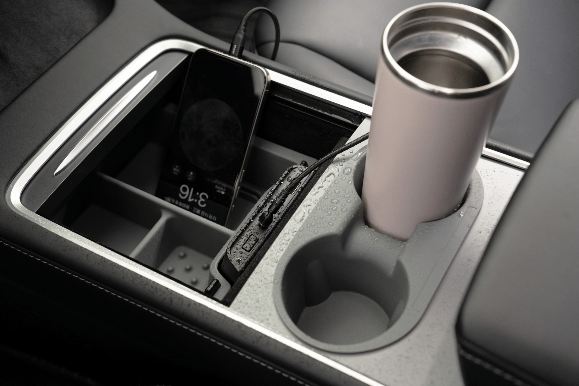 The JOWUA USB Hub for Tesla Model 3/Y, featuring dual USB-C 45W and LED warm light, is connected within a Model 3 center console. A smartphone displays 3:16 on its screen. In the cup holder rests a travel mug, with water droplets shimmering on the console's surface.