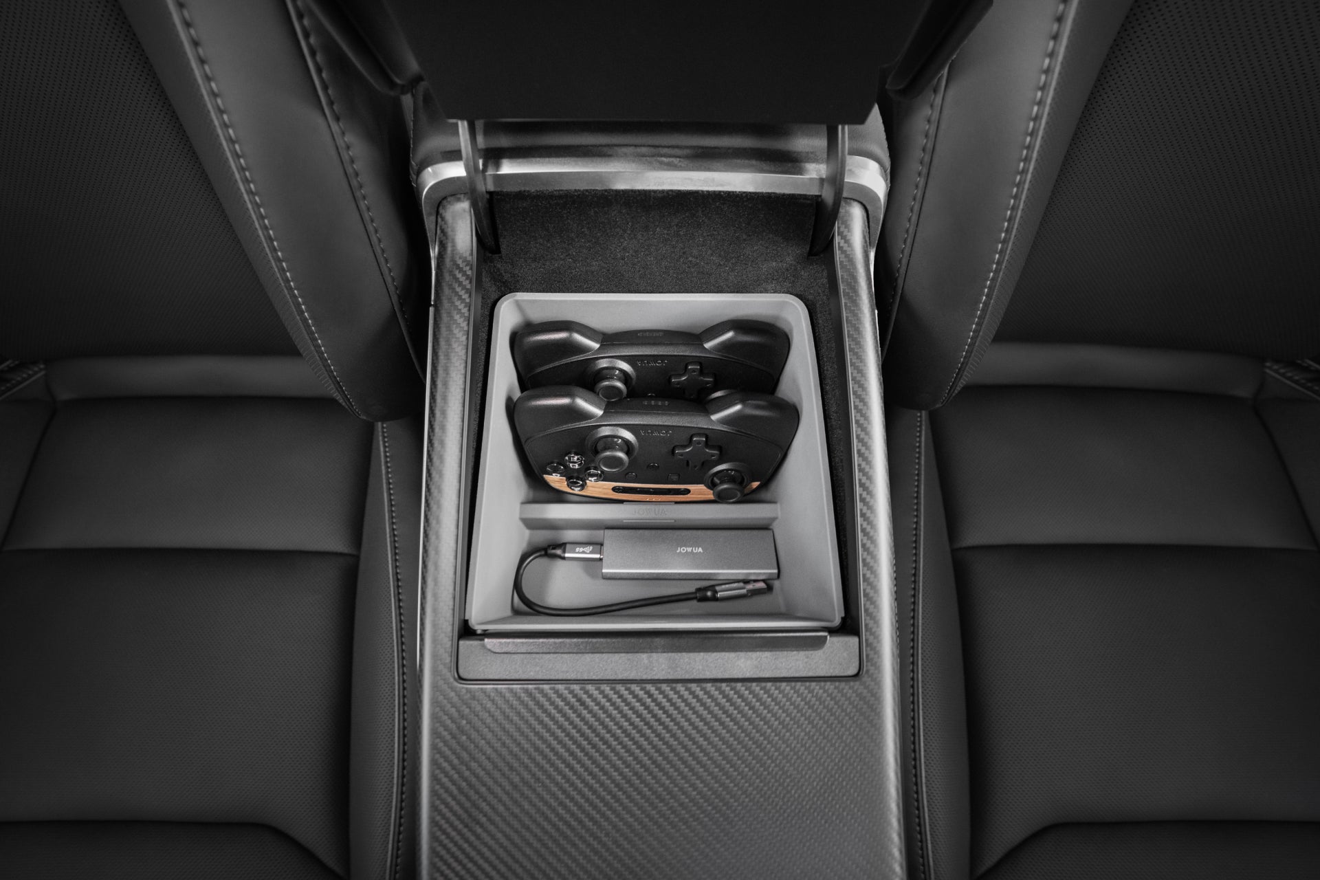 The interior view of the JOWUA Armrest Organizer for Tesla Model S/X features a rear compartment equipped to hold a video game controller, a small adapter, and a USB cable. The surrounding seats are expertly crafted from premium hybrid materials, with sleek black leather offering ultimate comfort and style.