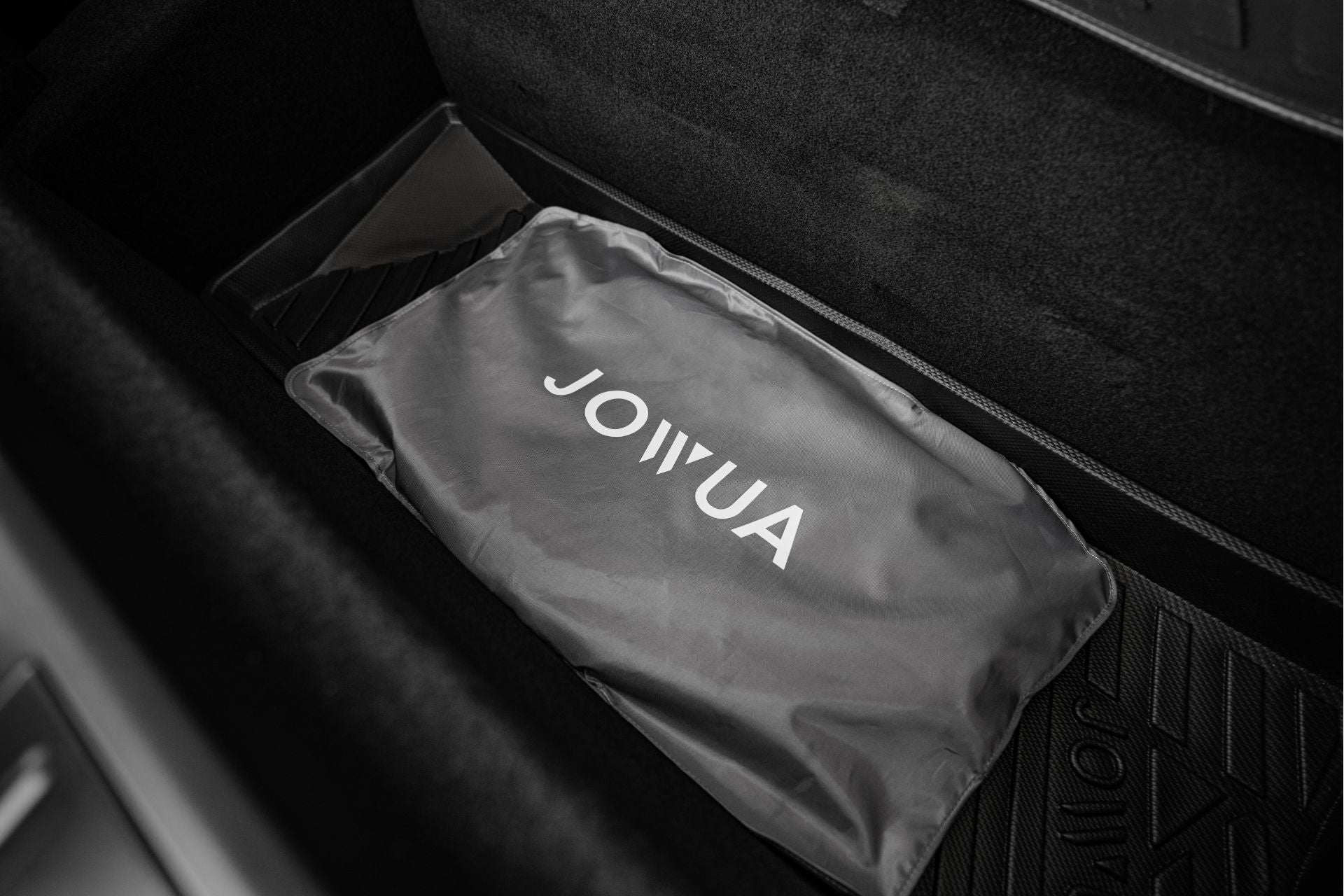 A black car trunk features a gray "JOWUA" branded bag, labeled as the Model S Glass Roof Sunshade, which is neatly placed on a protective mat. The bag offers UV protection and sits comfortably in the spacious trunk area.