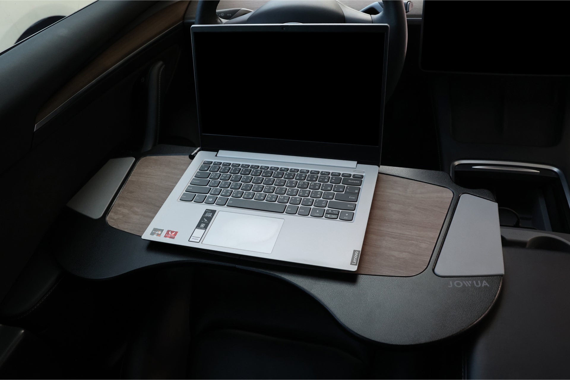 A 100W USB-C to Magnetic DC Charging Cable from JOWUA is neatly set on a wooden tray, crafted from high-quality material and attached to a car's steering wheel, forming an improvised workspace inside the vehicle. The tray is designed with a curved shape to perfectly complement the interior.