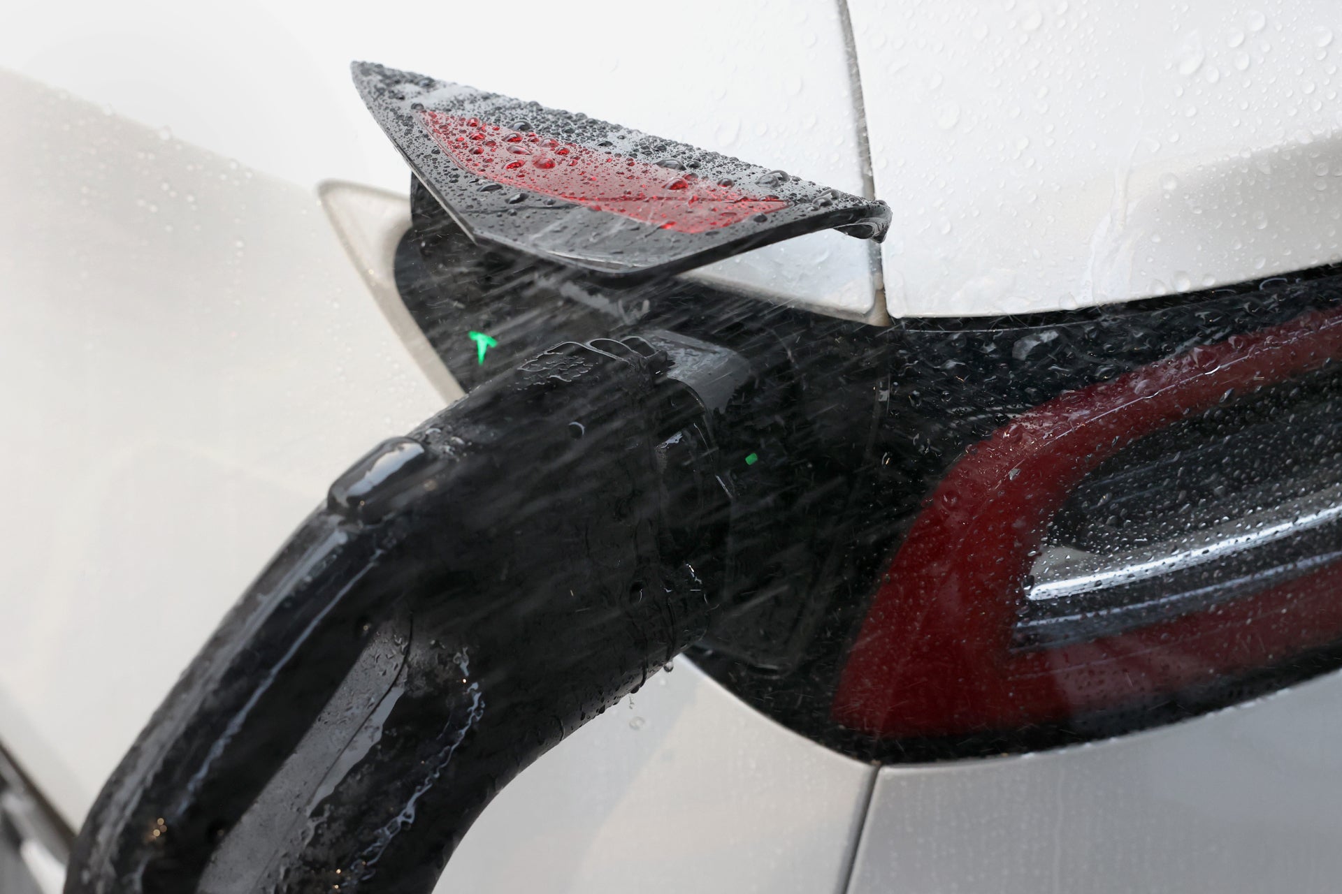 A close-up of a JOWUA CCS1 to CCS2 Adapter, with the cable securely connected to an electric vehicle charging port. The car is wet from raindrops, suggesting it might be raining, and captures the essence of sustainable travel even in adverse weather conditions.