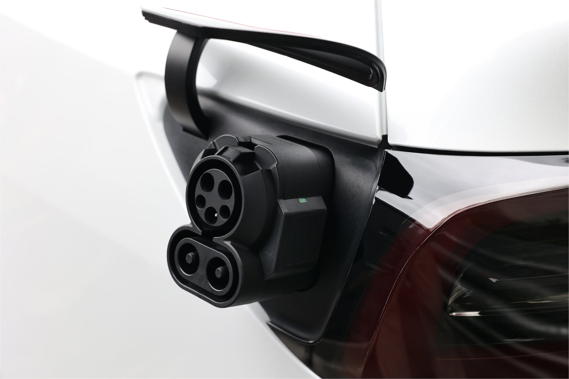 A close-up of an electric vehicle's charging port with a plug inserted using the JOWUA CCS1 to CCS2 Adapter. The sleek design of the adapter highlights advanced technology, seamlessly linking to the back of a white vehicle and demonstrating cutting-edge DC Fast Charging capabilities.