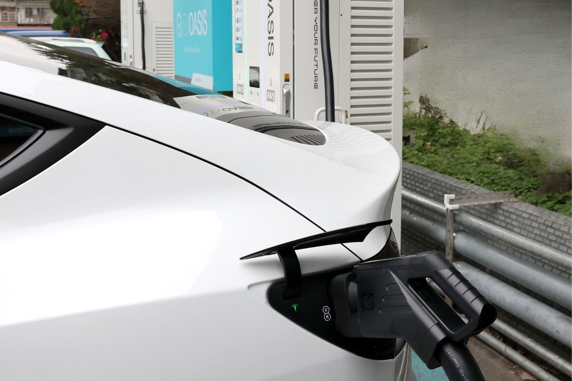 Close-up of a white electric car being charged with a JOWUA CCS1 to CCS2 Adapter at a DC Fast Charging station. The charging cable is plugged into the car's port. The background includes another vehicle and infrastructure related to CCS2 Electric Vehicles, showcasing advanced charging solutions for modern drivers.