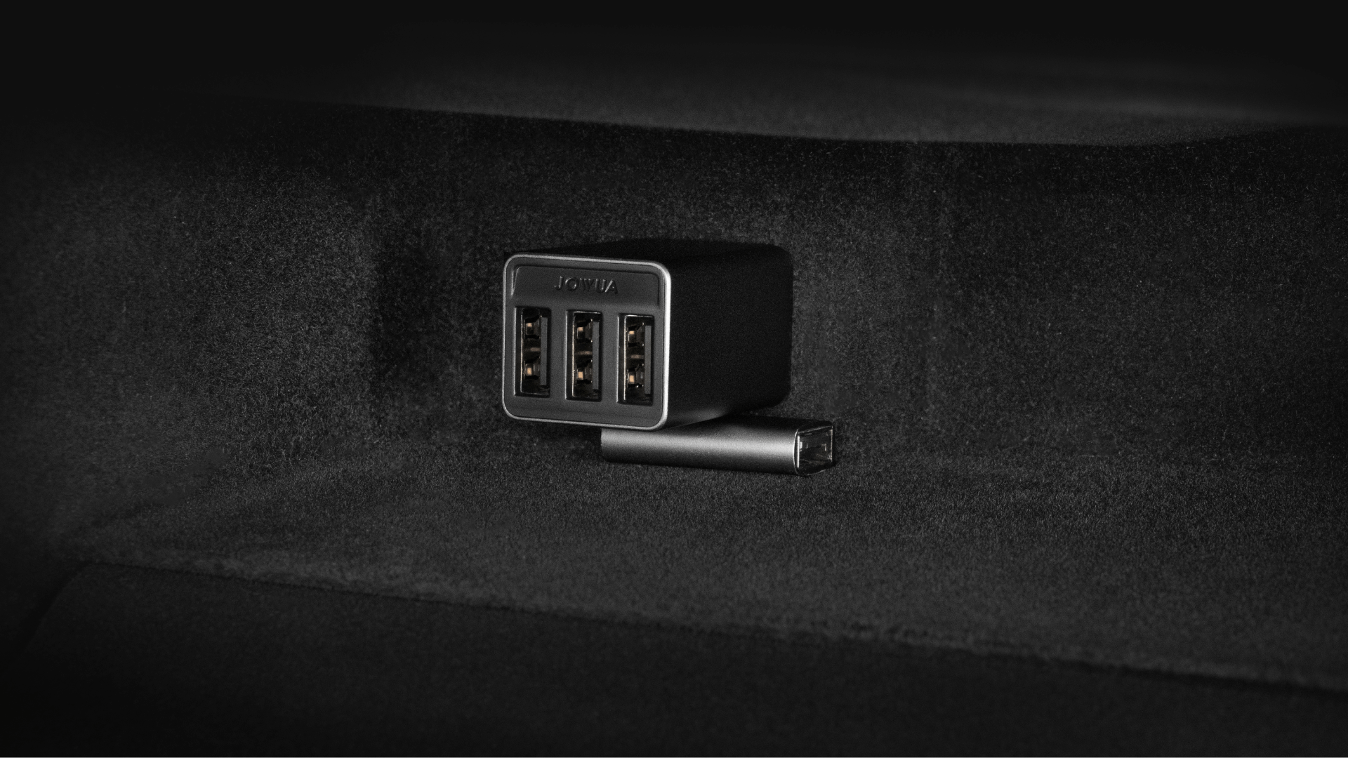 On a black fabric background, an elegant L-shaped USB-A Adapter from JOWUA for the Tesla Reengineered Model 3 Highland (2024+) is plugged into the socket. Its advanced design offers reliable charging convenience, making it an ideal companion for your Tesla drive to ensure all your devices stay powered up quickly and efficiently.