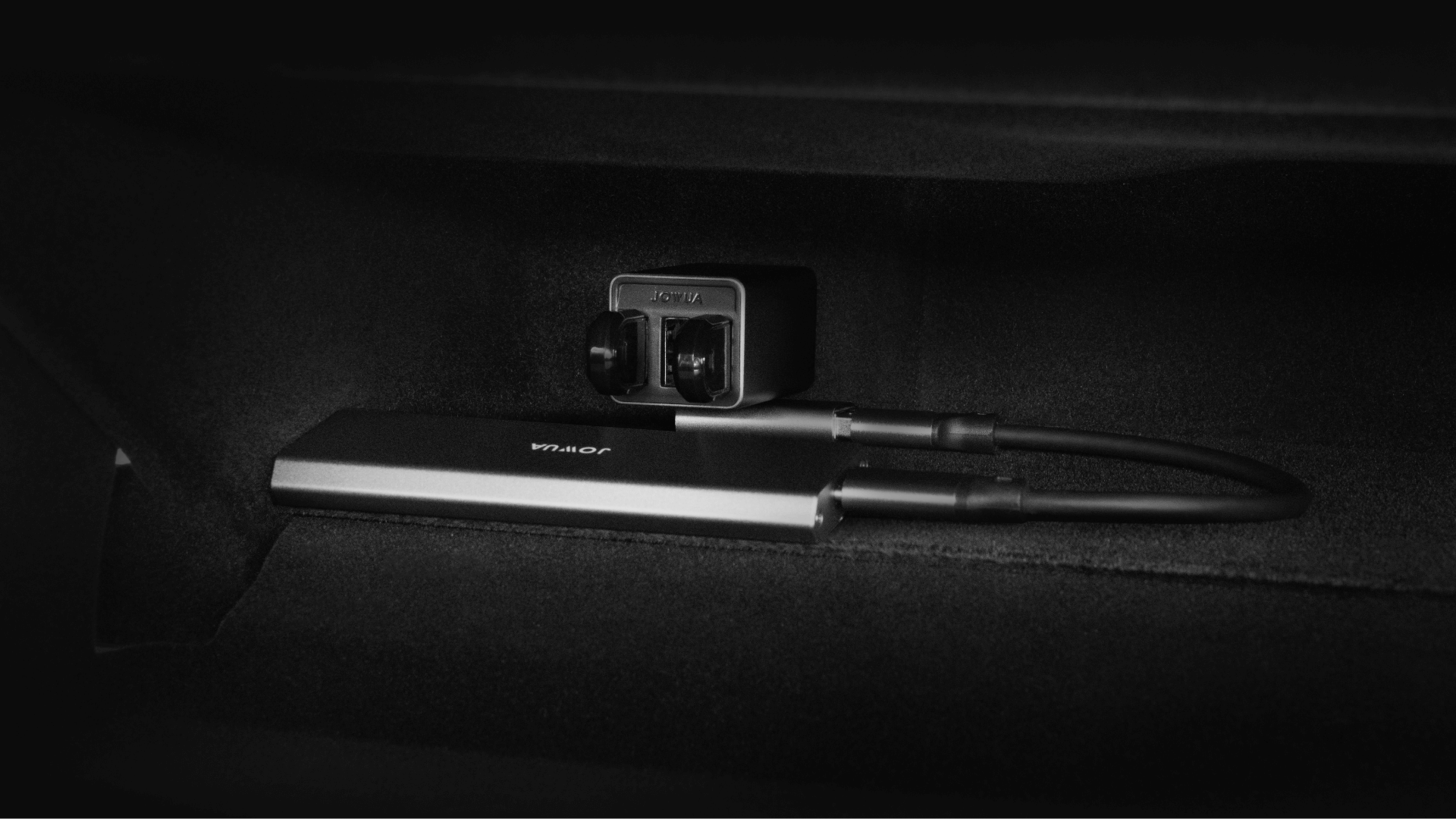 A sleek black device with two cables, showcasing a SuperSpeed USB connection, rests against a dark background. The L-shaped USB-A Adapter for the Tesla Reengineered Model 3 Highland (2024+) by JOWUA is plugged into a power outlet above the device, complementing its modern metal design.