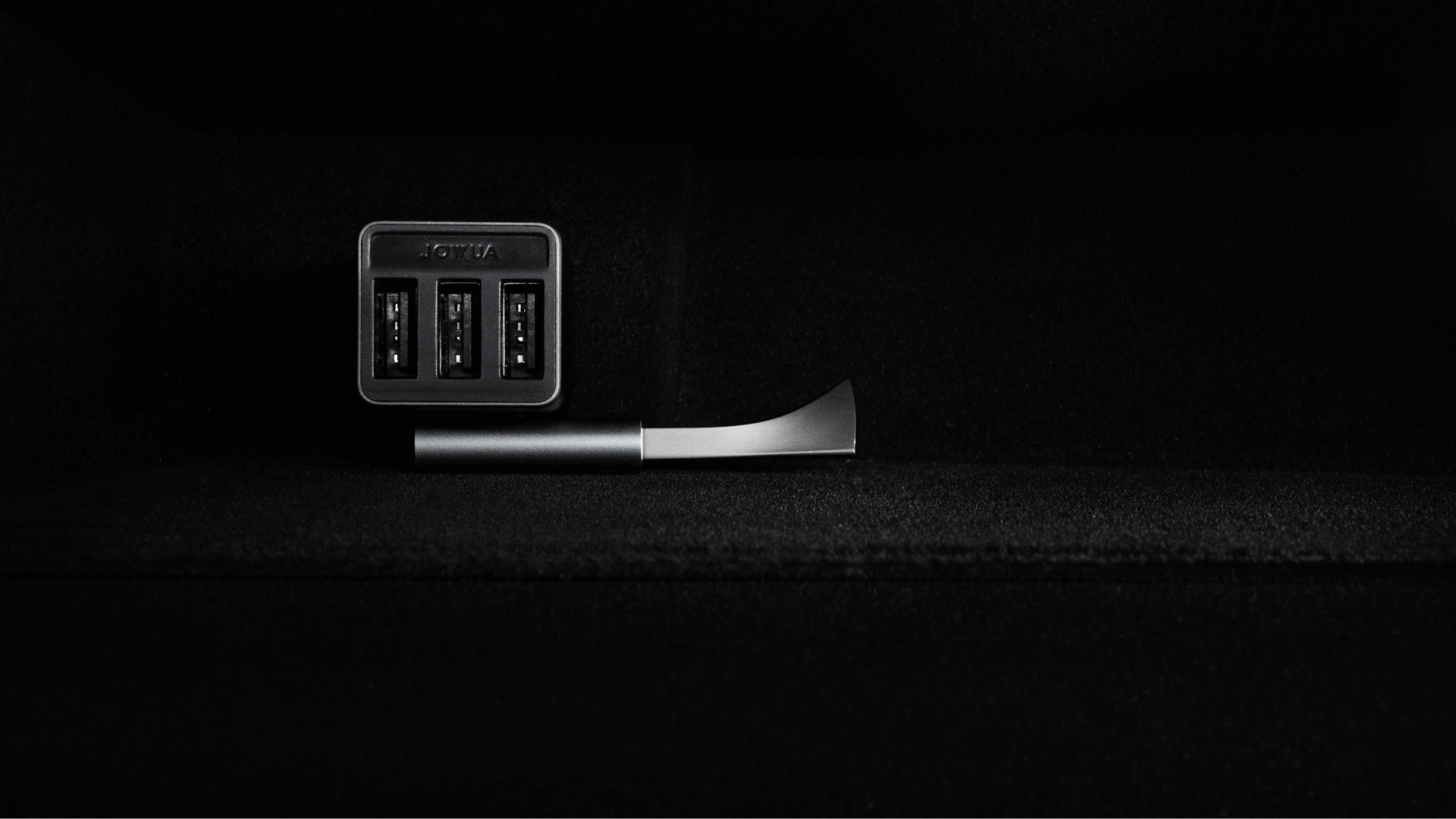 A minimalistic, dark-toned image showcases the sleek JOWUA L-shaped USB-A Adapter for the Tesla Reengineered Model 3 Highland (2024+), with its cutting-edge metal design. Featuring three SuperSpeed USB ports on the left side, the adapter's modern aesthetics are perfectly emphasized against a solid, dark background.