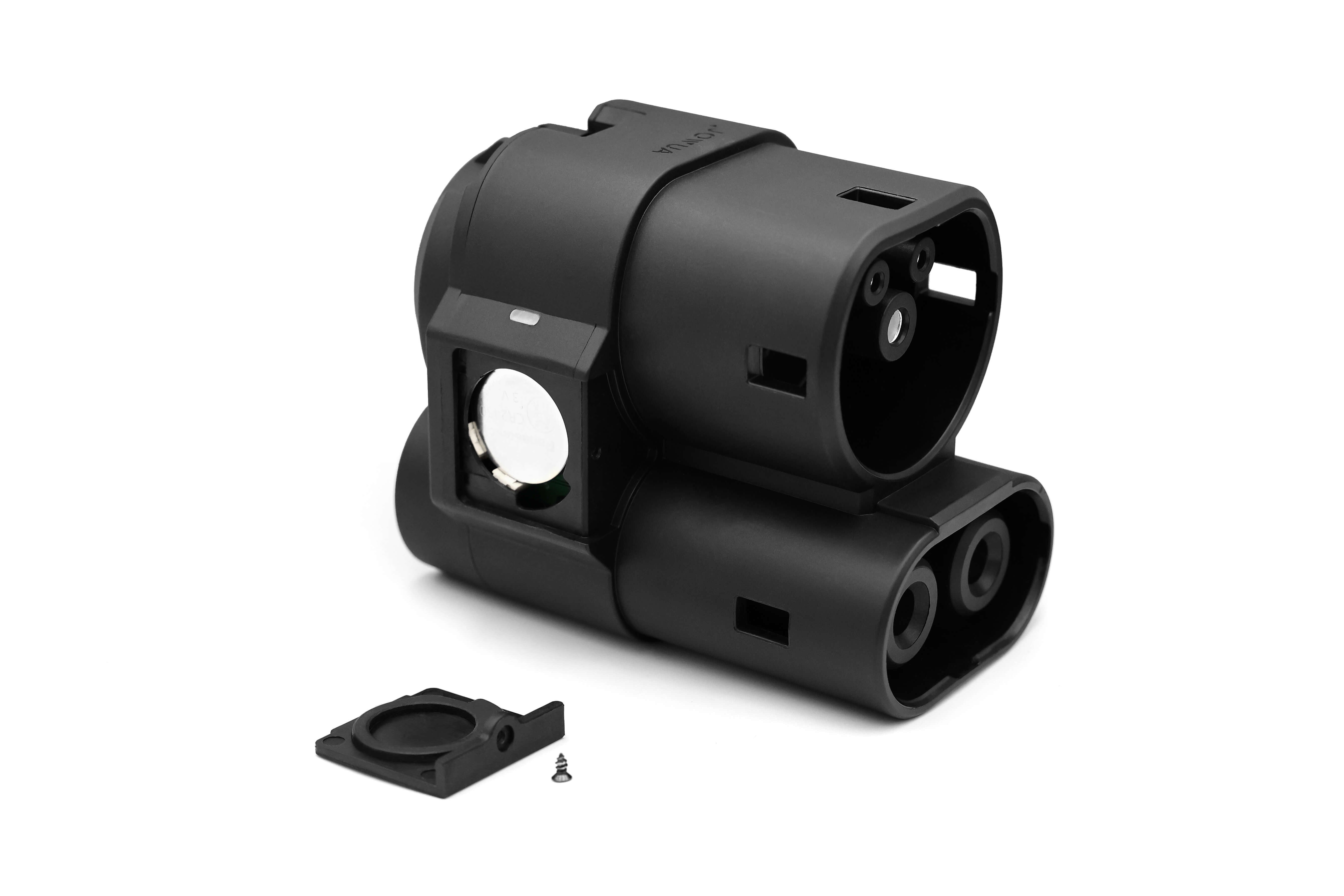 The JOWUA CCS1 to CCS2 Adapter is a black, rectangular electronic device casing featuring multiple openings and a circular silver component on the side, specifically designed for CCS2 Electric Vehicles. It comes with a detached black cover and a small screw placed beside it, ensuring easy maintenance access.