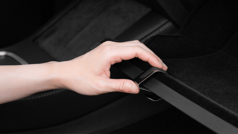 A hand secures a black seat belt connector in the vehicle, with dark upholstery in the background and a JOWUA Taiwan Hook Bundle (Model Y) seamlessly integrated into the car interior.