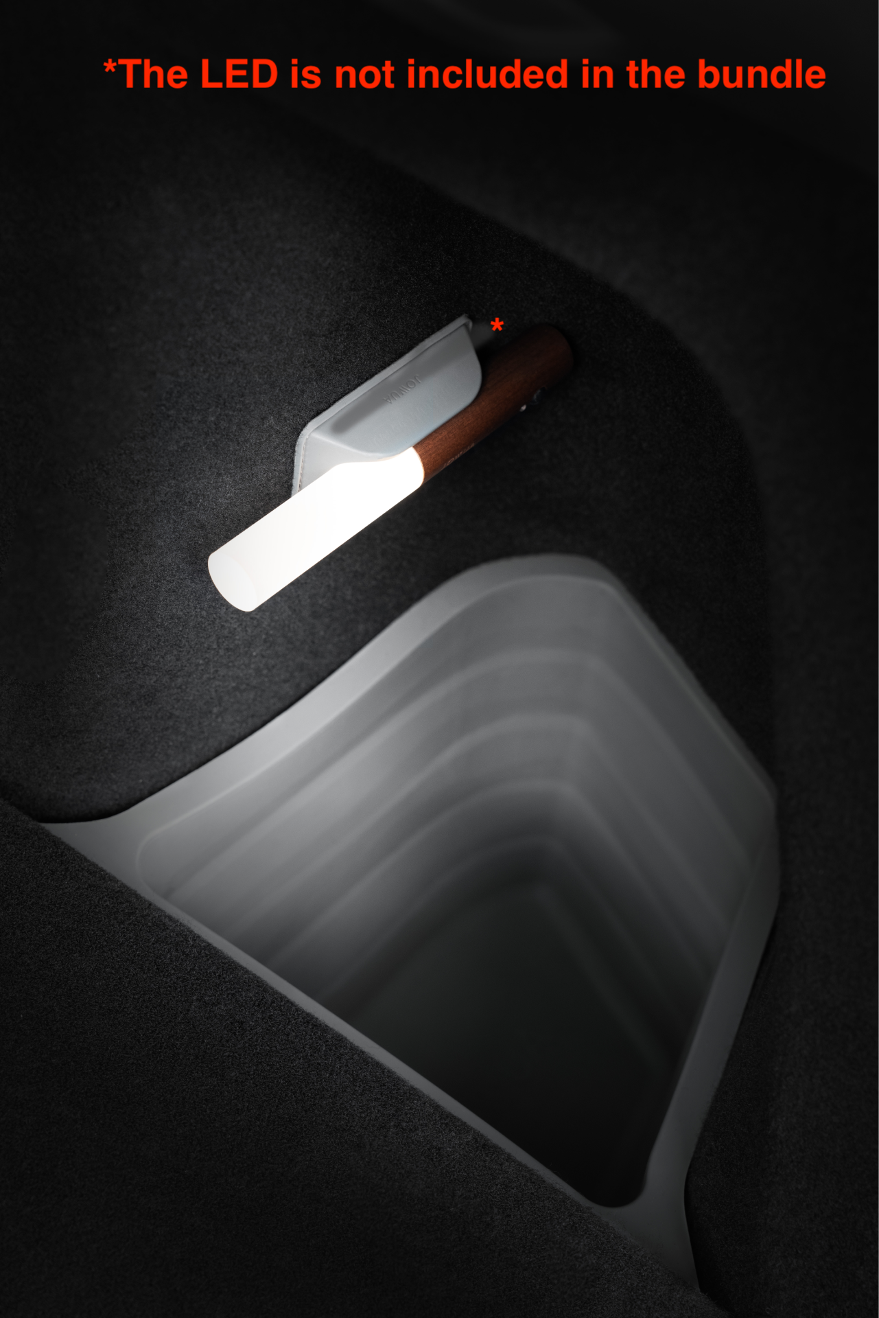 A JOWUA Model Y Trunk Combo flashlight with a modern, minimalist design and white light is mounted on a dark fabric surface, similar to Tesla Model Y trunk liners. In red letters above, it says, 