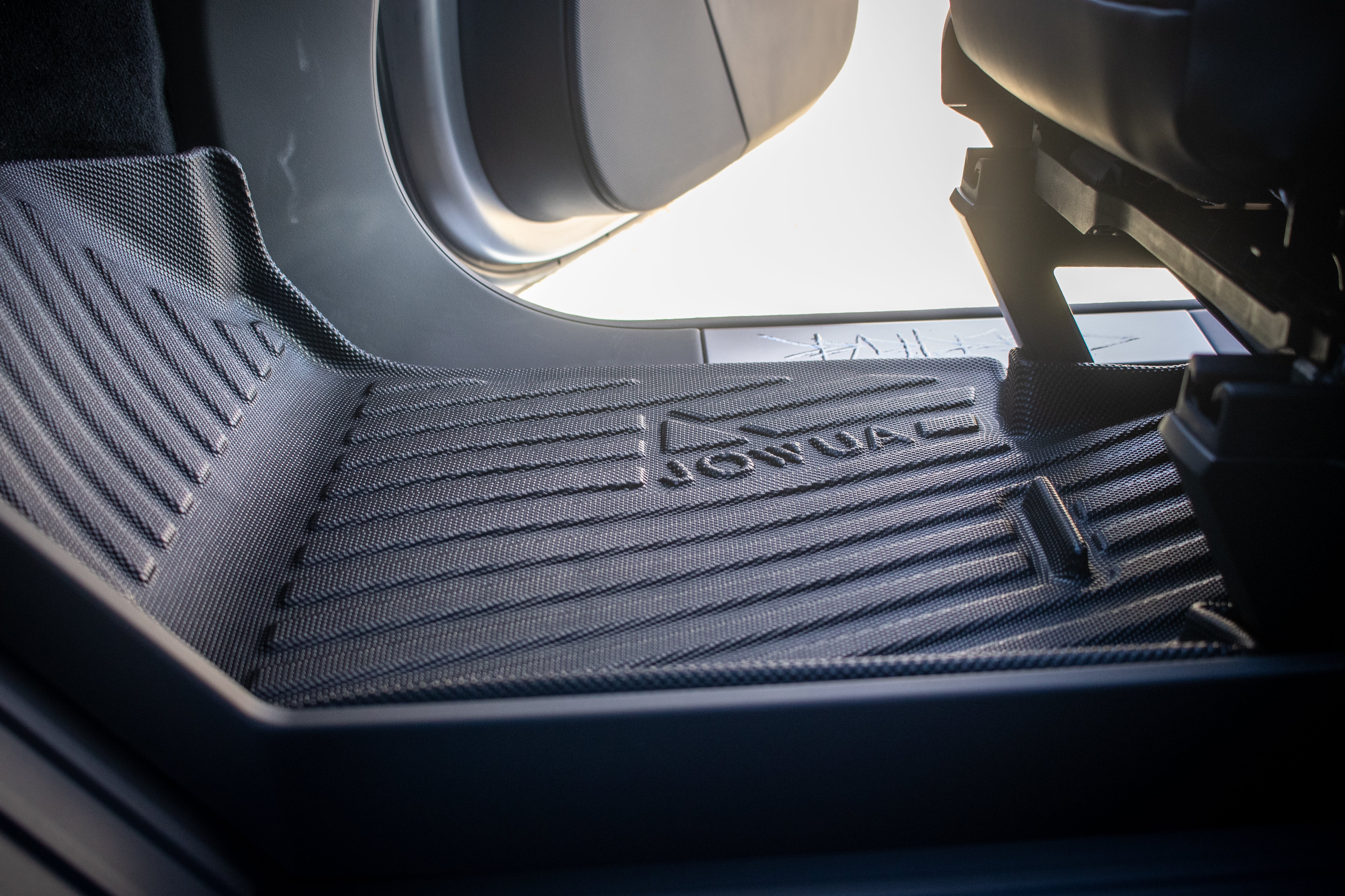 Close-up of a car's interior shows JOWUA's All Weather Floor Liners for the Tesla Cybertruck. The textured liner, labeled 