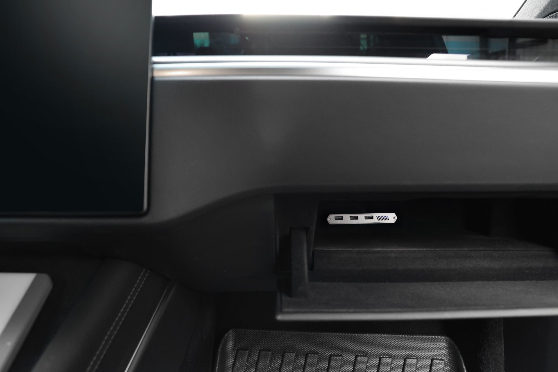 The image reveals the interior of a Tesla Model S, featuring a glove compartment equipped with a JOWUA 3-Port USB DashCam Hub (1TB NVMe SSD). The dashboard is enhanced by a touchscreen display, and the floor is adorned with a textured rubber mat for added grip.