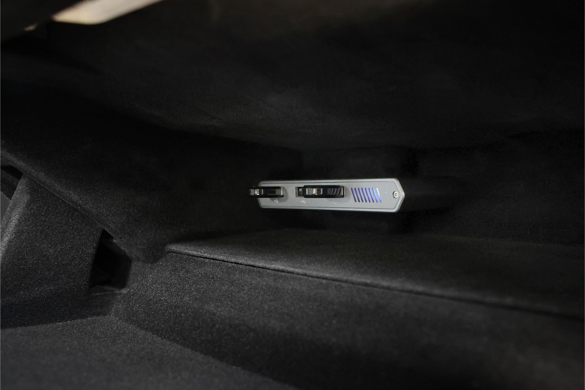 A close-up of a Tesla Model S interior reveals a 3-Port USB DashCam Hub (1TB NVMe SSD) from JOWUA mounted under the dashboard. This sleek, modern device features a SuperSpeed+ High-Efficiency Storage display and multiple slots, contrasting with the dark material surrounding it.