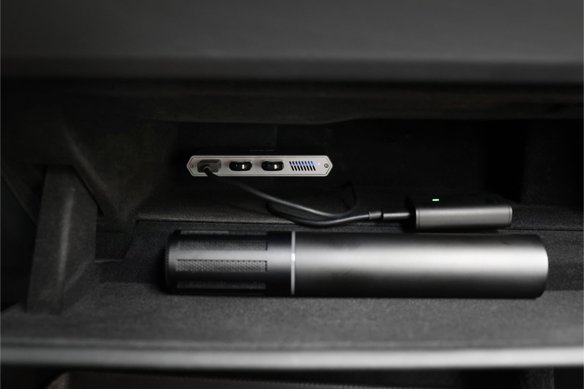 The JOWUA 3-Port USB DashCam Hub (1TB NVMe SSD), resembling a data transmission port, is securely housed within a cylindrical compartment. Linked by a cable featuring a green LED indicator, this SuperSpeed+ high-efficiency storage device rests on felt lining, crafted to organize these electronics neatly.