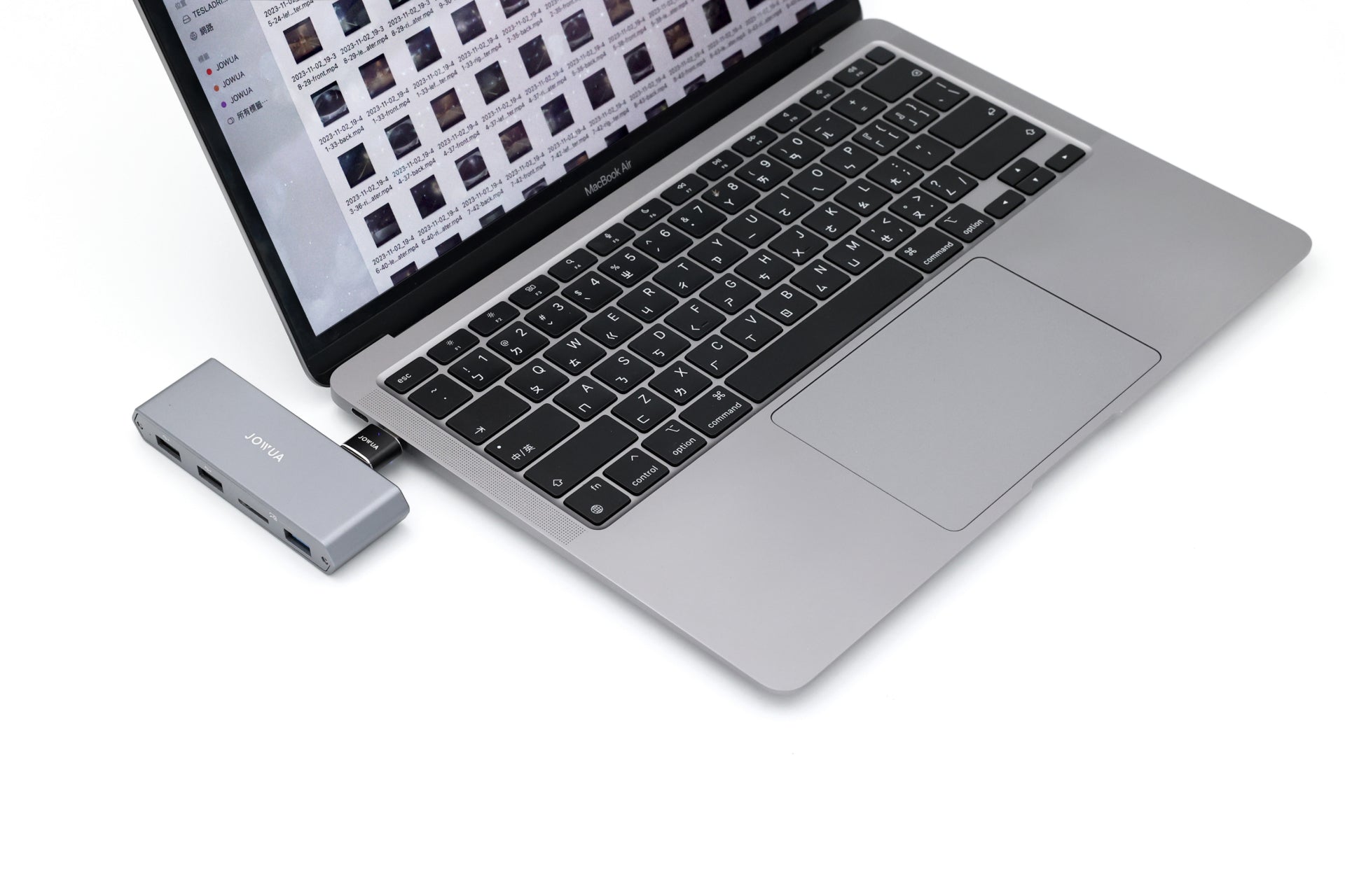 A silver laptop open to a screen displaying photo thumbnails is connected to the JOWUA 3-Port USB DashCam Hub (MicroSD Reader) V2, offering impressive USB expansion with multiple ports. The device, ideal as a Tesla accessory, rests on a white surface.