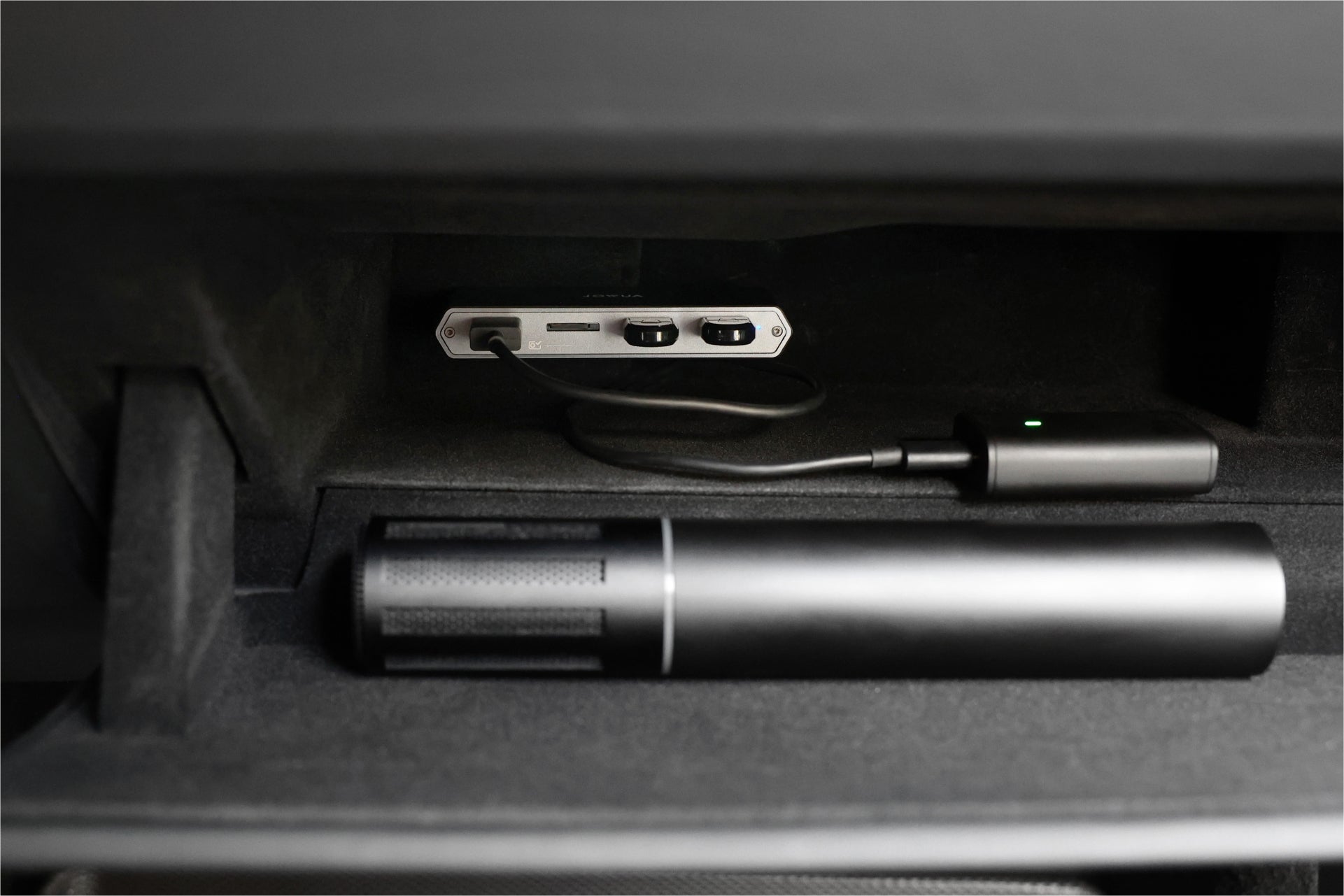 The glove compartment contains the JOWUA 3-Port USB DashCam Hub (MicroSD Reader) V2 installed at the back, complete with a connected power adapter. Alongside a black cylindrical object, it is engineered for efficient heat dissipation to ensure seamless operation without interference from GPS signals.