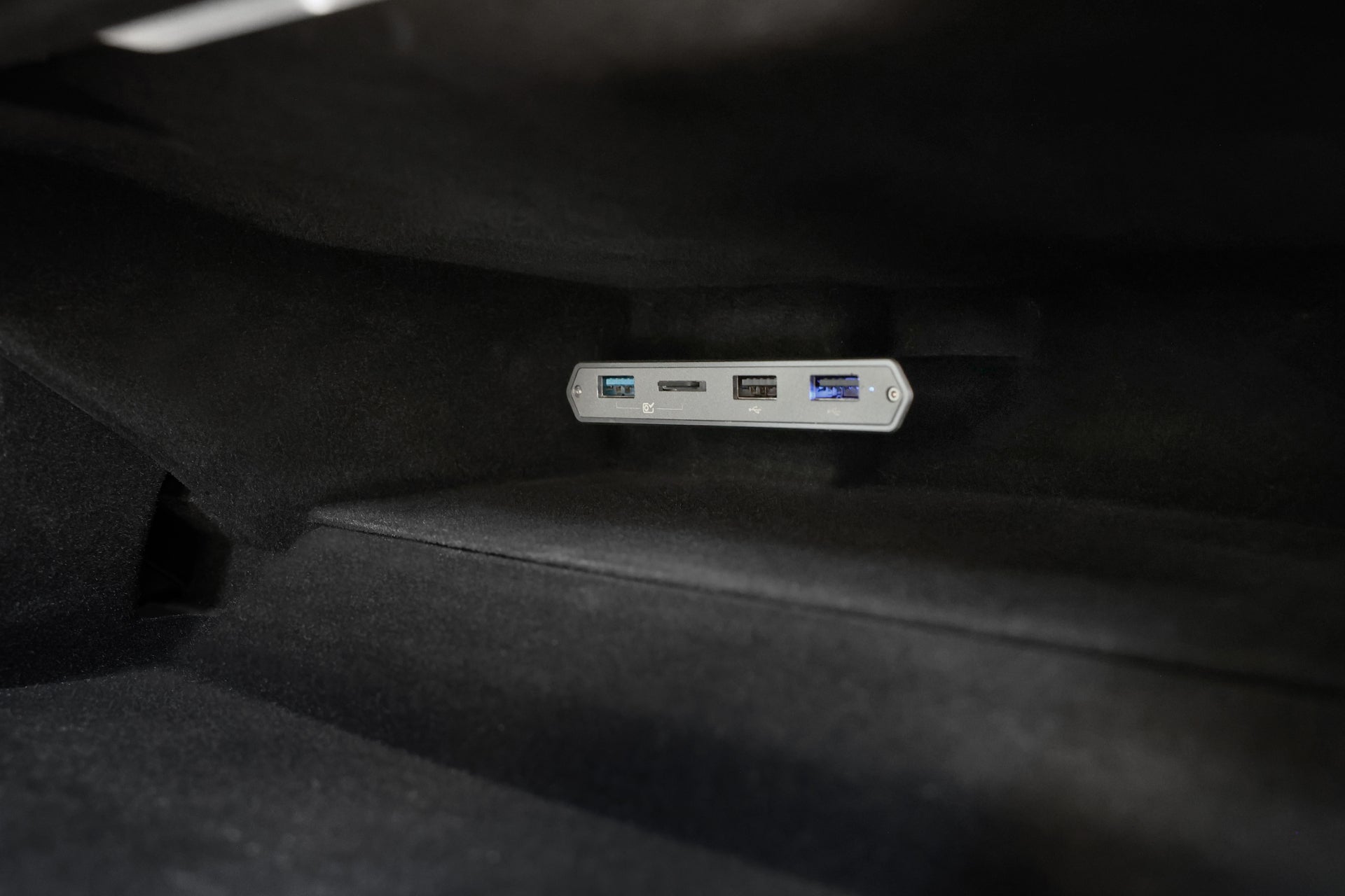 A close-up view of a gray panel inside a vehicle's spacious glove compartment showcases the JOWUA 3-Port USB DashCam Hub (MicroSD Reader) V2, which includes Tesla Owners’ Data Port alongside USB 2.0 and USB 3.0 connections, all set against a dark interior background.