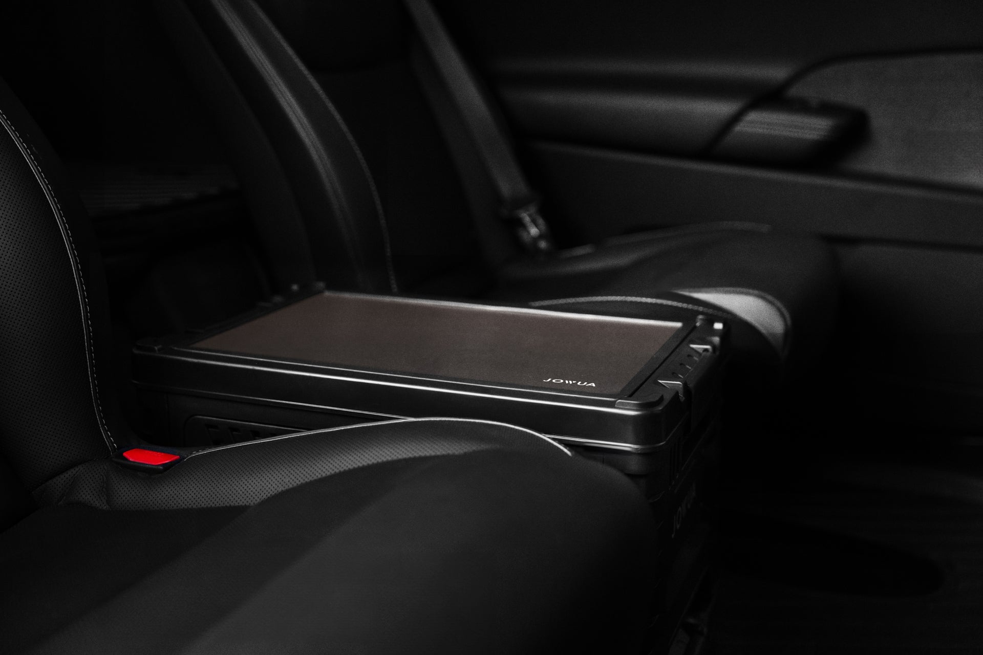 A JOWUA 30L Stackable Storage Box and Trunk Organizer for Teslas rests on the backseat of a car, neatly beside a rugged laptop. The vehicle's dark upholstery and visible seatbelt suggest a secure and practical workspace setup, enhanced by this rear seat storage solution that keeps essentials within easy reach.