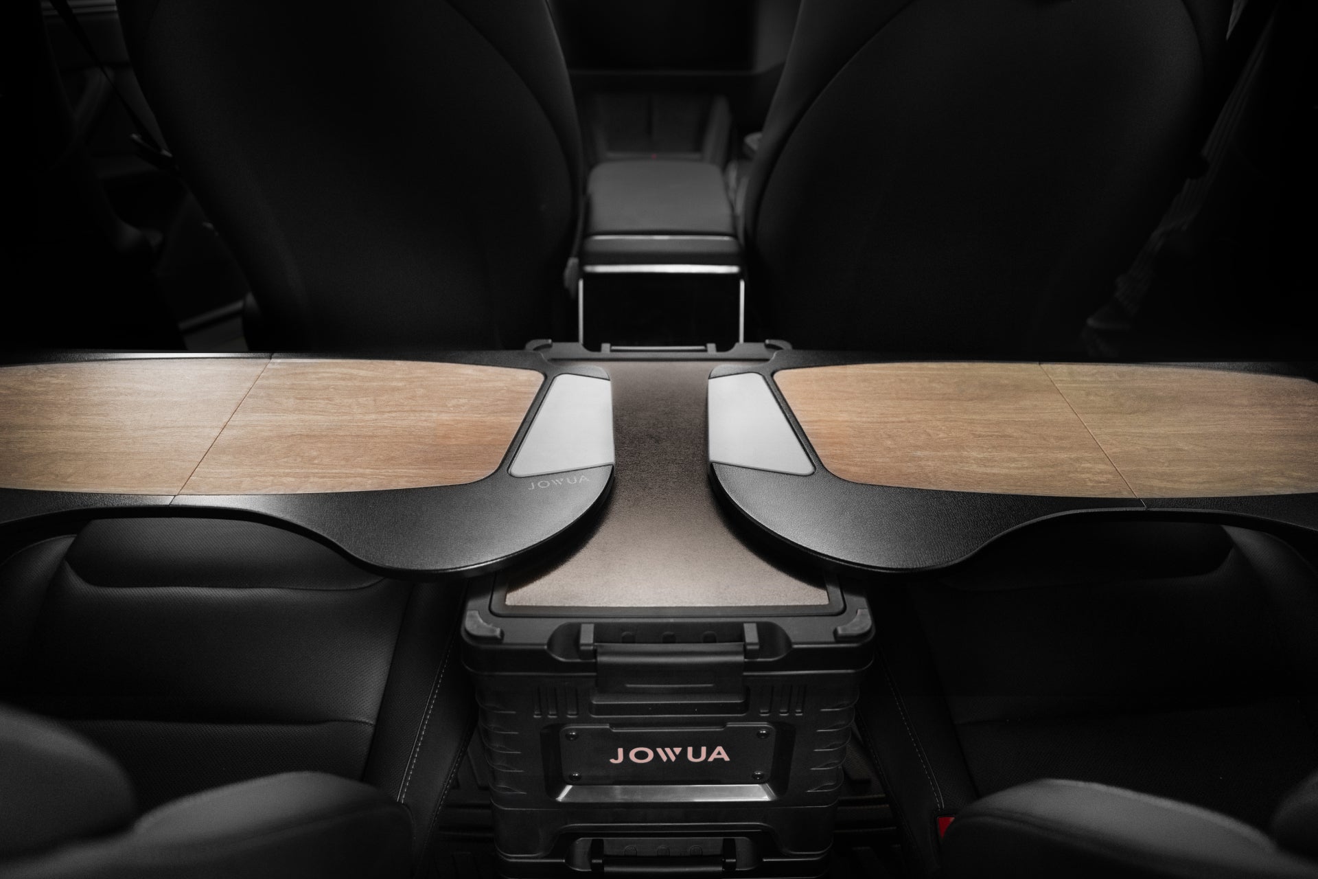 The interior of a vehicle includes a JOWUA branded 30L Stackable Storage Box and Trunk Organizer designed for Teslas. Wooden trays are attached on either side, forming a split-level surface over the central console area between the front seats, reminiscent of a car interior tool with its sleek functionality.