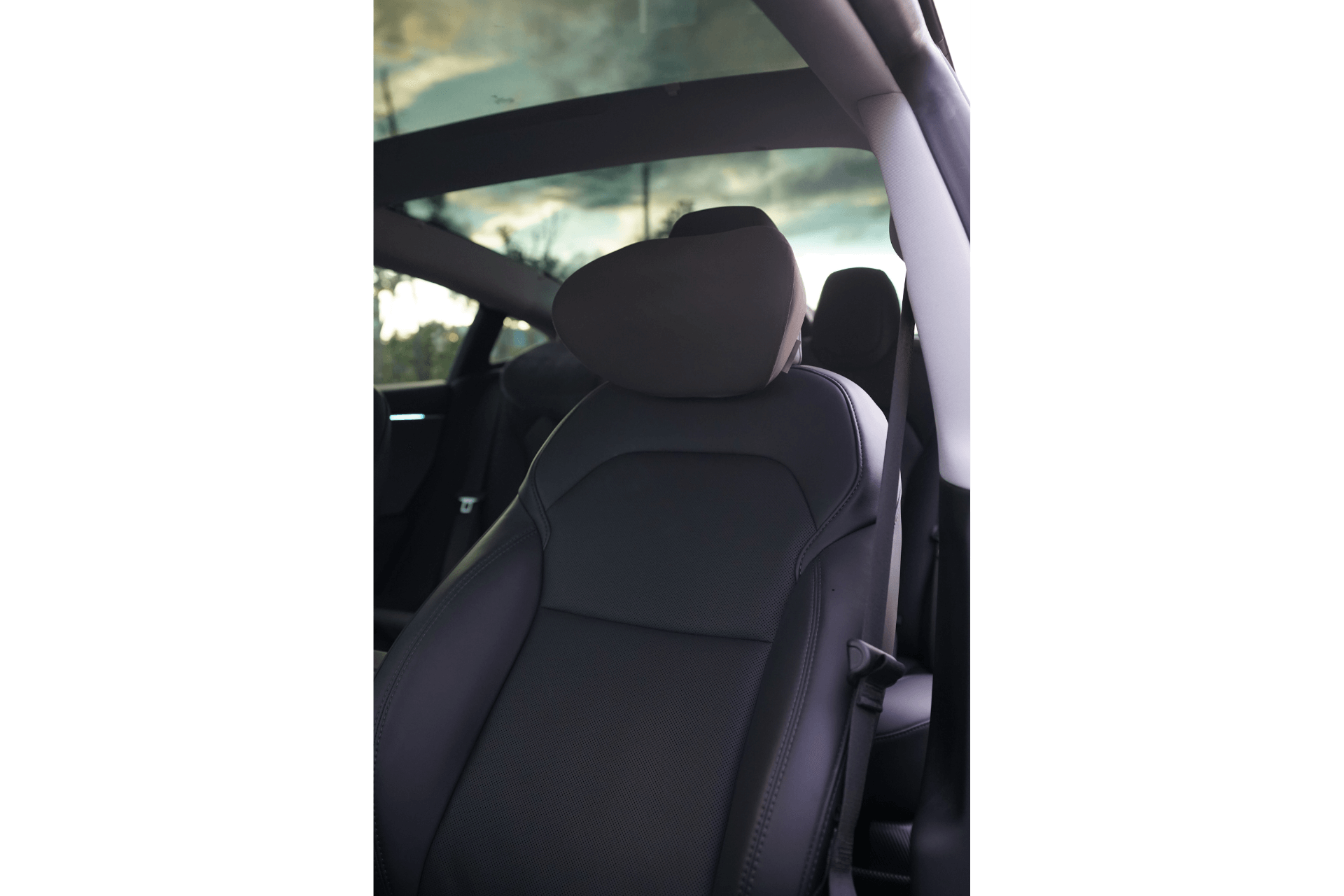 The JOWUA Car Neck Pillow on the driver's seat, designed with ergonomic features and adjustable height, showcases black upholstery with a prominent headrest and part of the seat back visible. The open glass sunroof reveals a cloudy sky, enhancing the spacious and airy feel of the vehicle's interior.