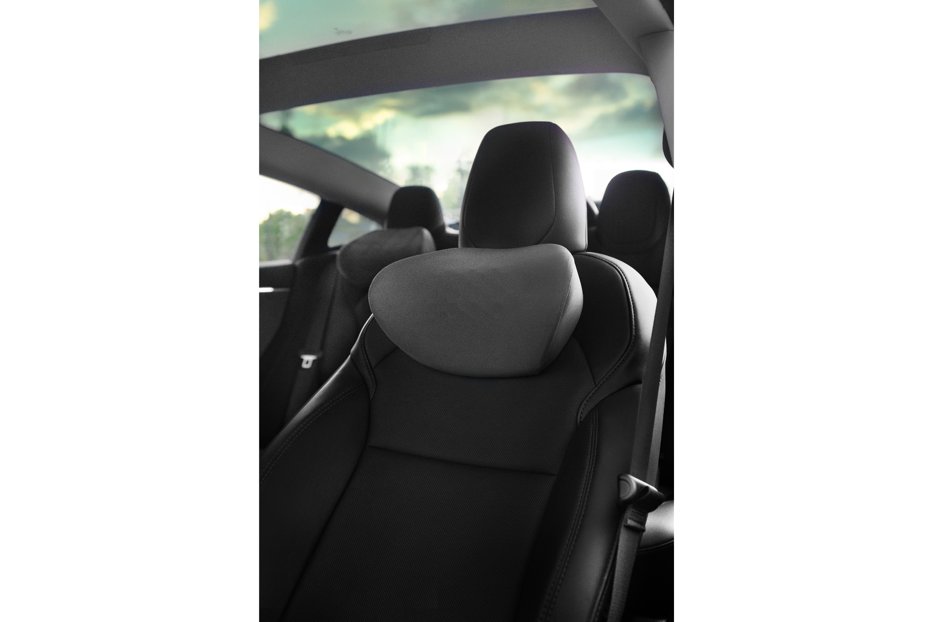 Interior view of a car highlighting the ergonomic design of the front seat under a panoramic sunroof. The seat, upholstered in dark fabric, features adjustable height settings, while the sky with clouds is beautifully visible through the sunroof. Enhance your comfort with the Car Neck Pillow by JOWUA.