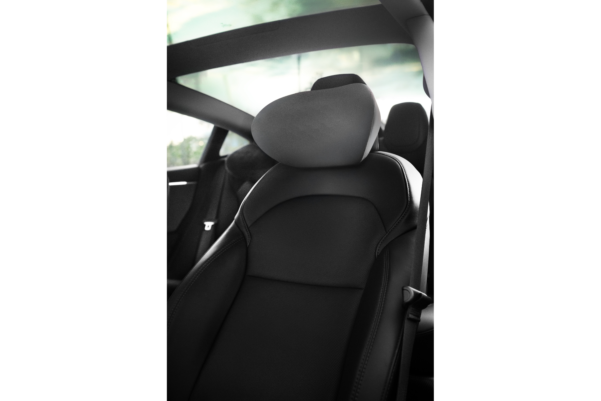 A close-up of a modern car's interior features the sleek black leather seat complemented by the JOWUA Car Neck Pillow with an ergonomic design. The background reveals part of the car window, offering a glimpse of greenery outside.