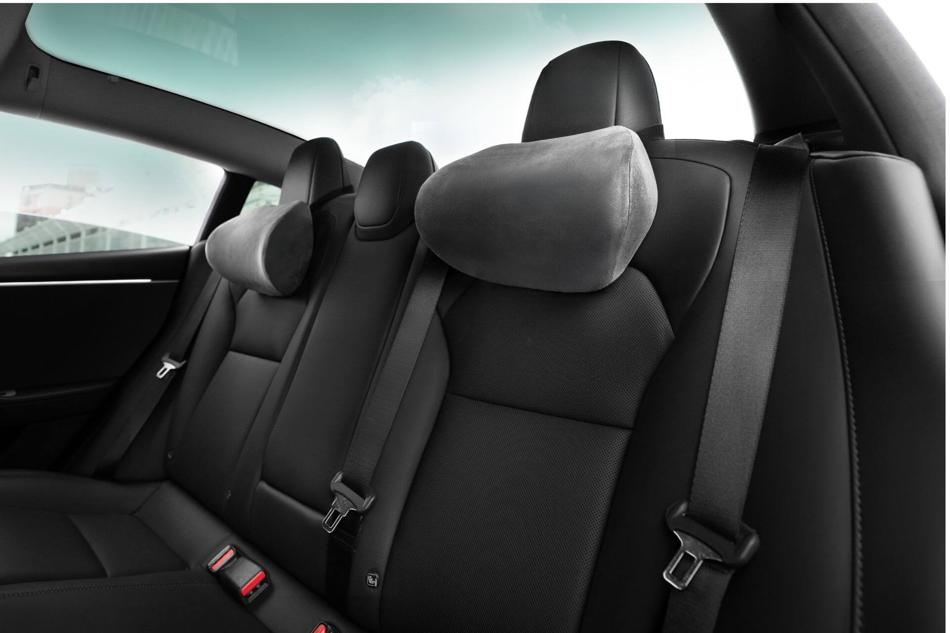 The car's interior highlights JOWUA neck pillows on ergonomic black rear seats with dual-material design, adjustable height headrests, and visible seat belts, set against a cloudy sky view through the windows.