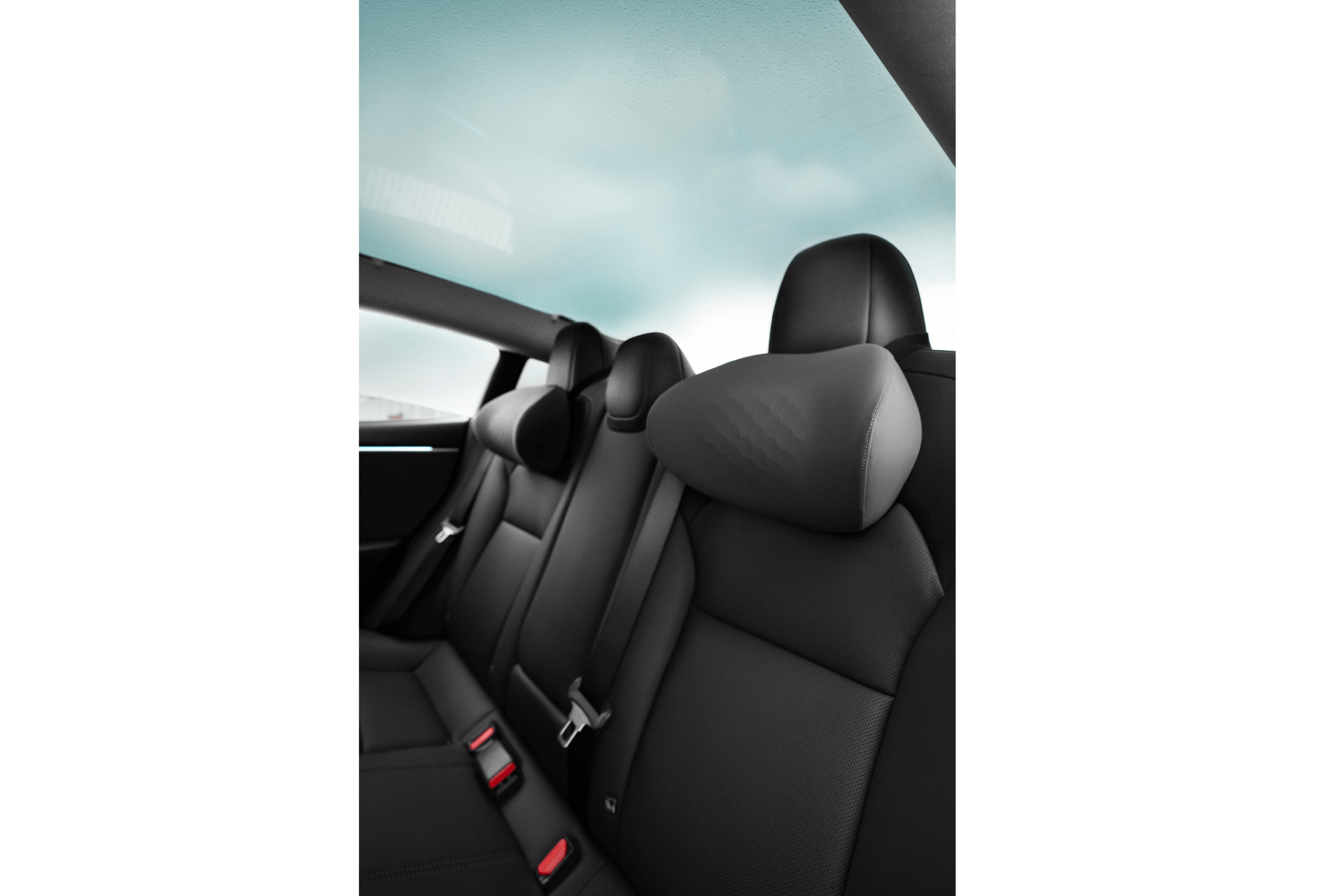 Interior view of a car's back seat, featuring sleek black leather upholstery with ergonomic design. Adjustable headrests complement the seatbelt fasteners, enhanced by the JOWUA Car Neck Pillow for added comfort, while a large glass roof displays a cloudy sky.