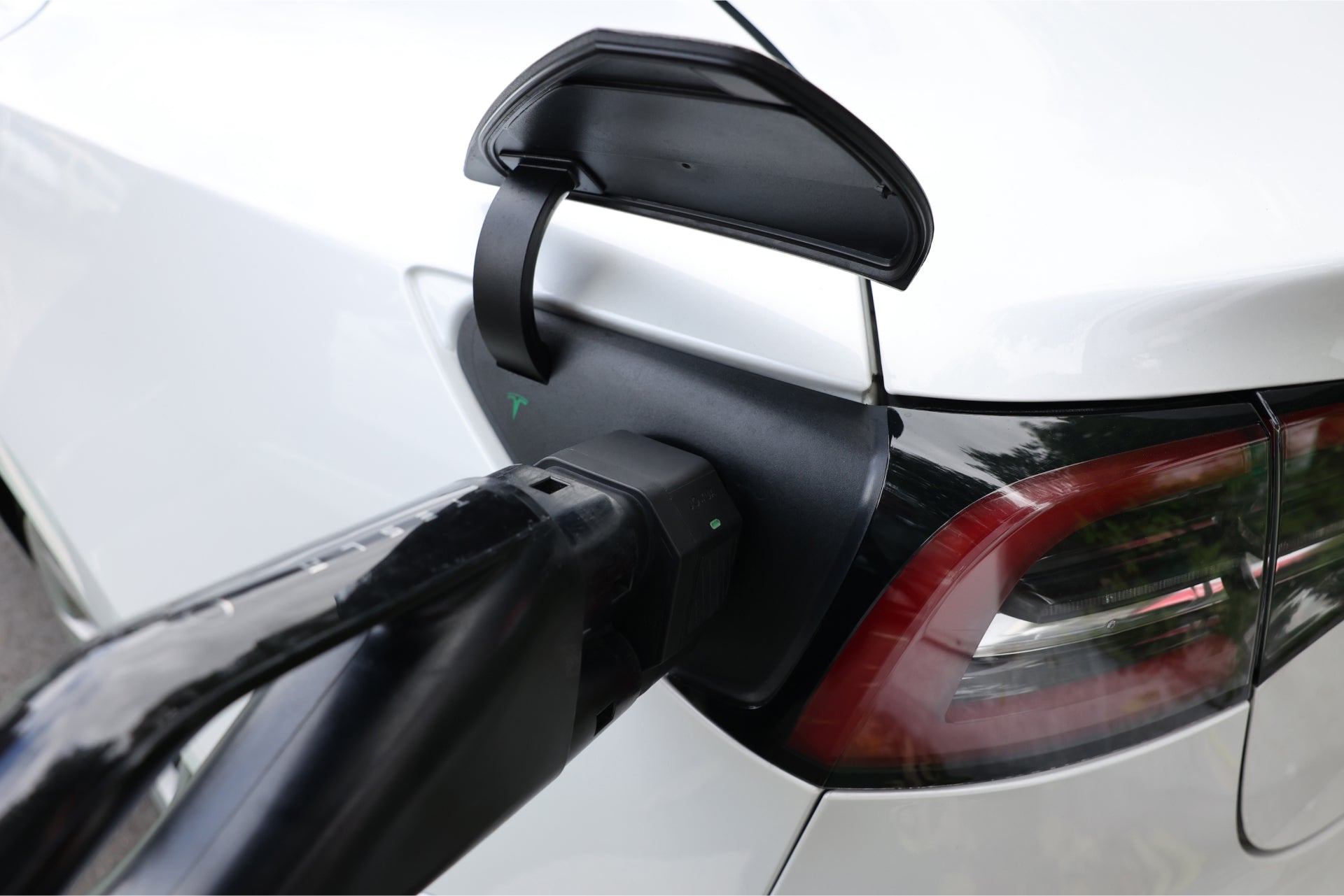 A white electric car is being charged with the JOWUA CCS2 to NACS DC Charging Adapter. The cable connects to the open port near the tail light for seamless DC Fast Charging.