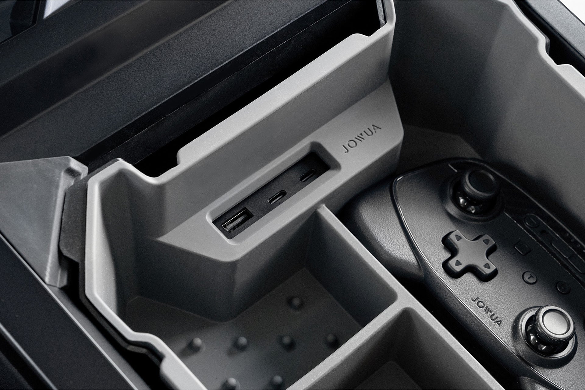 A close-up of a gray JOWUA Center Console Set for Tesla Cybertruck shows its storage compartment with USB charging stations and slots for gaming controllers. The organizer includes premium silicone sections and efficiently holds a black controller.