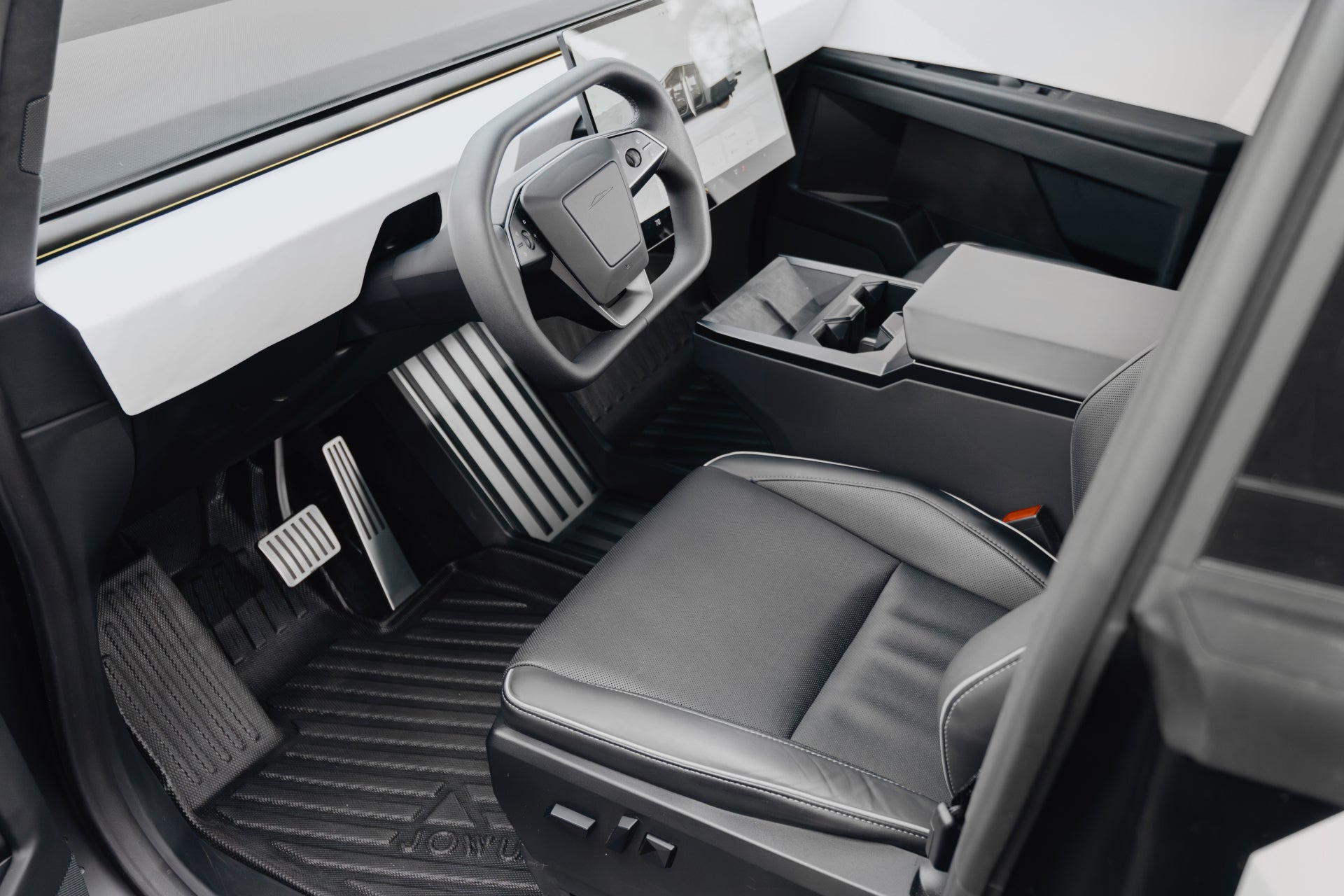 The Tesla Cybertruck's futuristic interior features a minimalist design with a large display and angular steering wheel, complemented by black leather seats. JOWUA's All Weather Floor Liners enhance durability with their geometric pattern, reminiscent of high-quality liners.