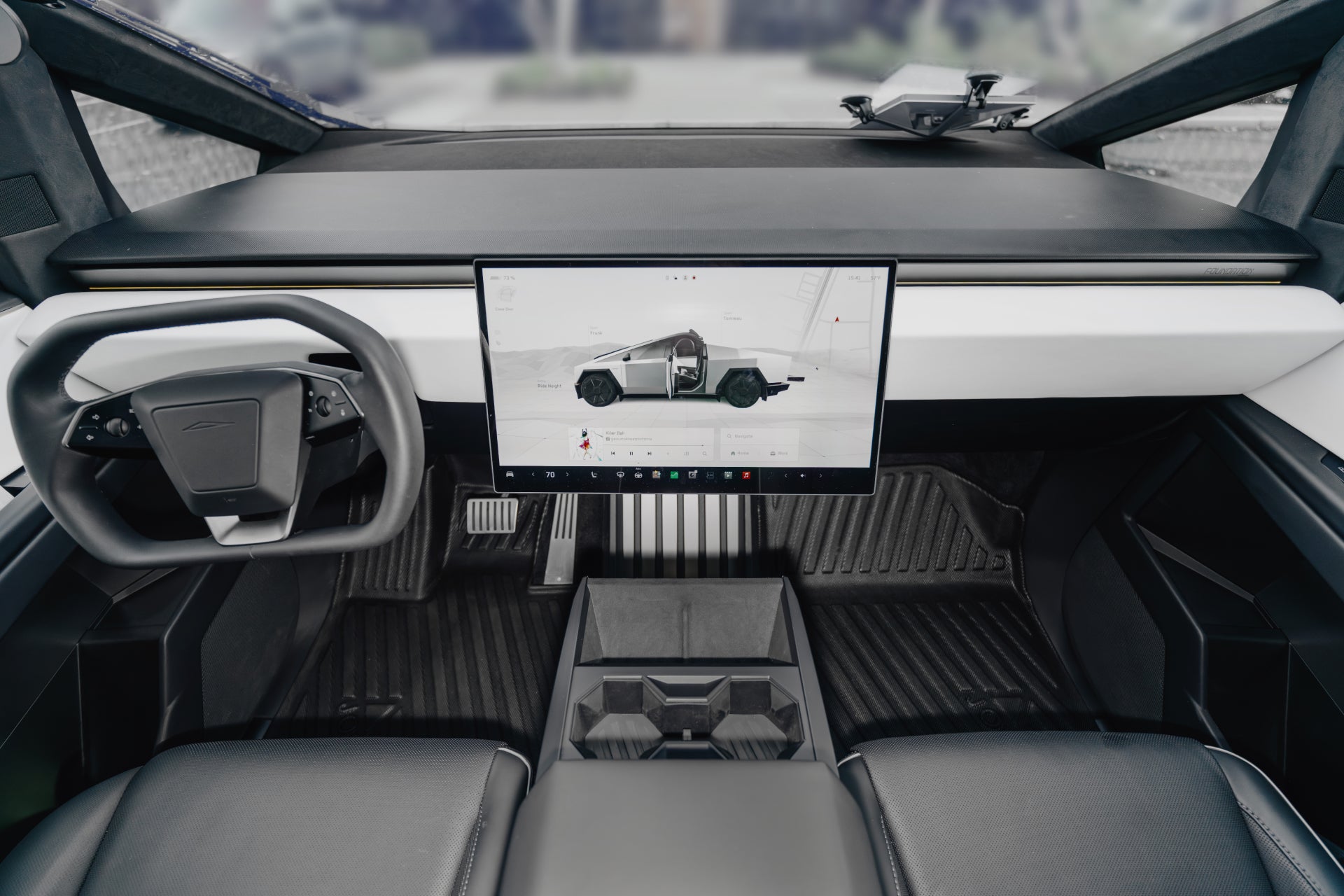 The image showcases the futuristic interior of a Tesla Cybertruck with a minimalist design, featuring a rectangular steering wheel, central touchscreen display, sleek dashboard, dark seating, and enhanced durability thanks to JOWUA's All Weather Floor Liners.