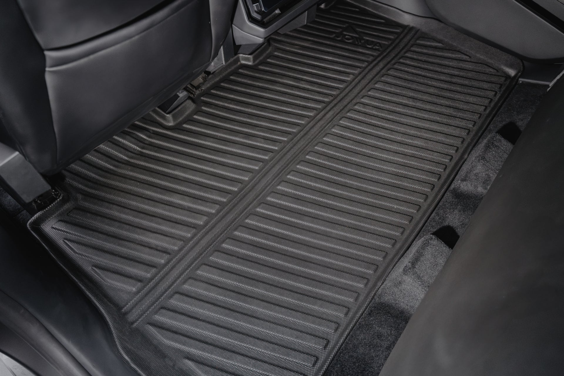 A close-up of a Tesla Cybertruck’s rear interior reveals JOWUA All Weather Floor Liners. These black rubber mats feature a grooved, non-slip texture and are cleanly placed over the carpet, with glimpses of the seats and door panels.