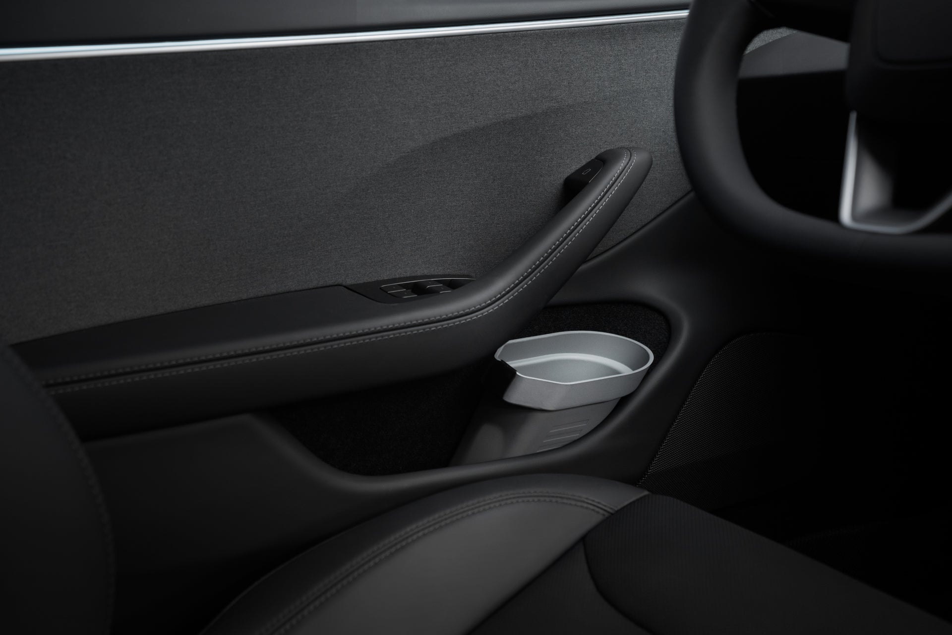 Close-up of a car's interior door panel, highlighting a sleek, modern design with black leather upholstery, a silver door handle, and an integrated cup holder. The JOWUA Door Side Storage Box (Set of 2) enhances the Tesla Model with its innovative storage bin crafted from premium silicone material for enhanced durability and style.