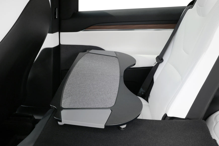 The interior of a car highlighting the rear seating area includes a retractable armrest equipped with the JOWUA Foldable Car Tray for Tesla, complete with a fabric cover. The seats are upholstered in premium PU leather complemented by black and wood trim accents, offering a modern and sleek atmosphere ideal for fans of the Tesla Model S/3/X/Y.