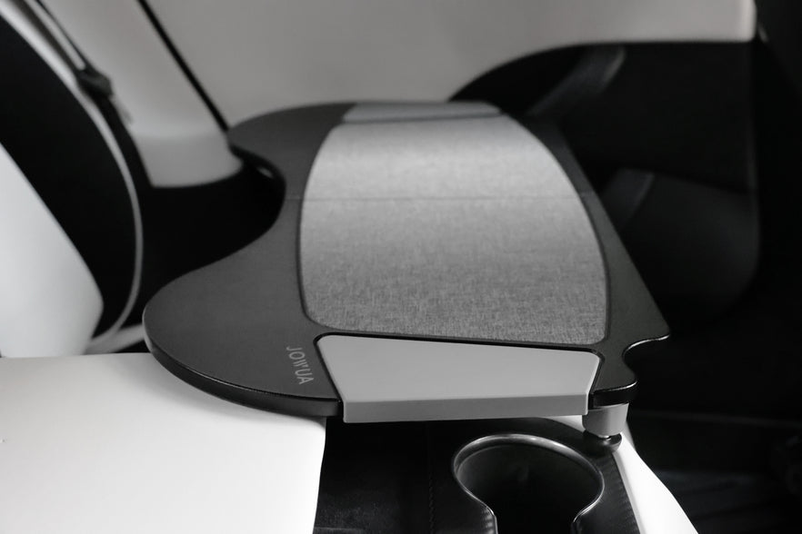 The interior of the Tesla Model S includes a foldable car tray from JOWUA, crafted from premium PU leather with a gray textured surface. Positioned beside a white seat and above a cup holder, it beautifully combines functionality with sleek design that aligns seamlessly with Tesla's innovative spirit.