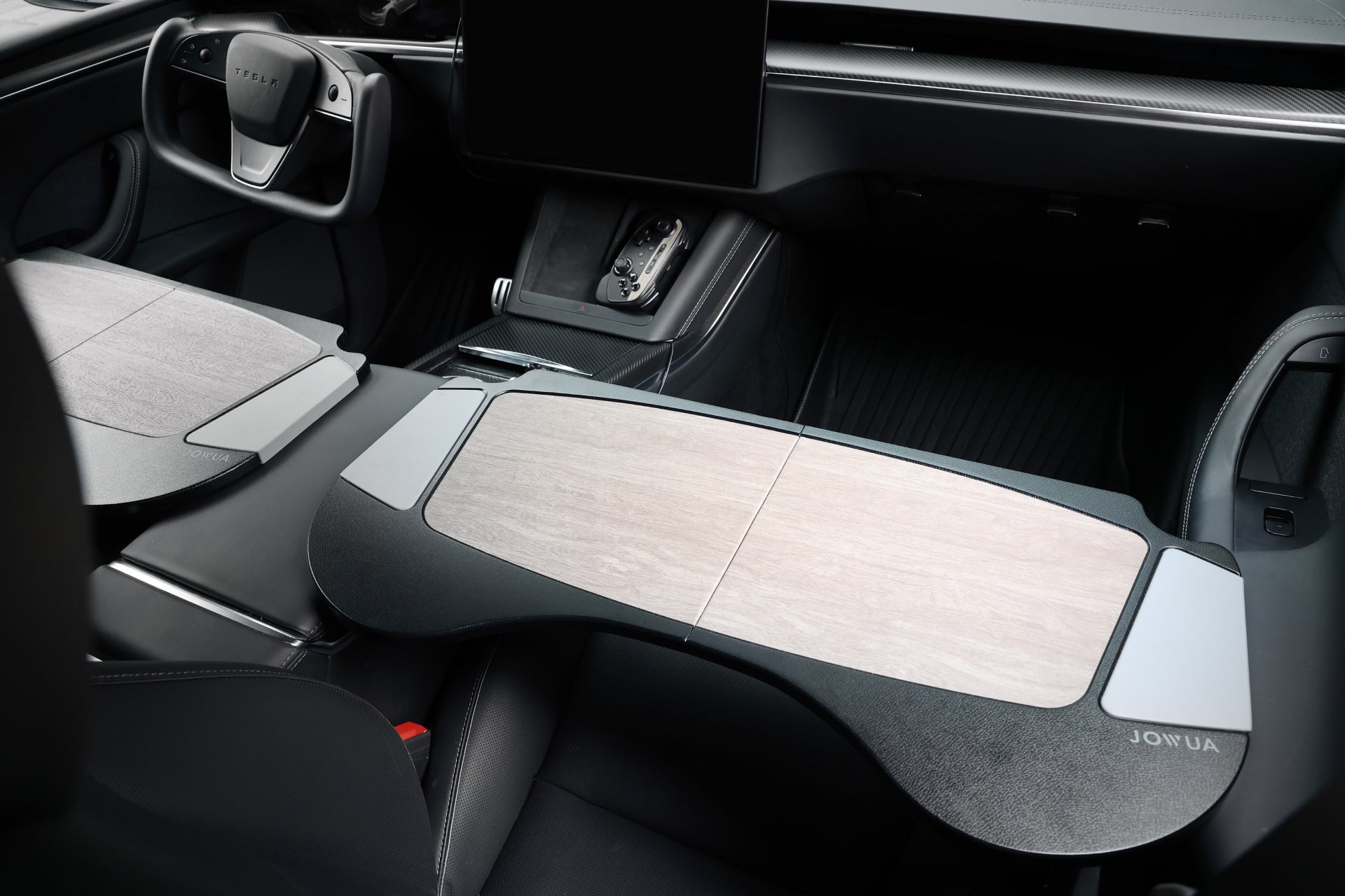 The interior features a sleek, modern steering wheel paired with the JOWUA Foldable Car Tray for Tesla, finished with a wooden design that spans across the front seats. Premium materials refine the center console, which is equipped with various controls and a large touchscreen. The accessory is complemented by black leather seating.