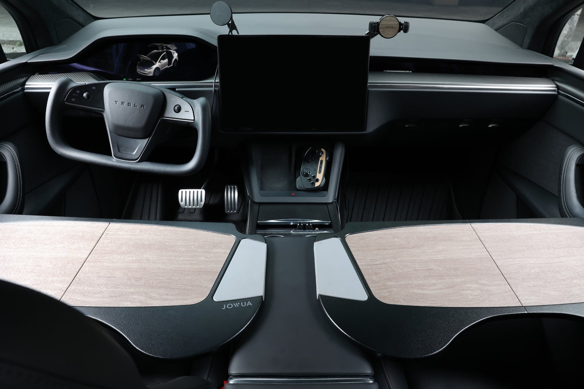 The interior of a Tesla showcases a minimalist design with premium materials, including a steering wheel, large central touchscreen, and wood-accented dashboard. In this modern and sleek setting, the JOWUA Foldable Car Tray perfectly complements the gear selector and two pedals.