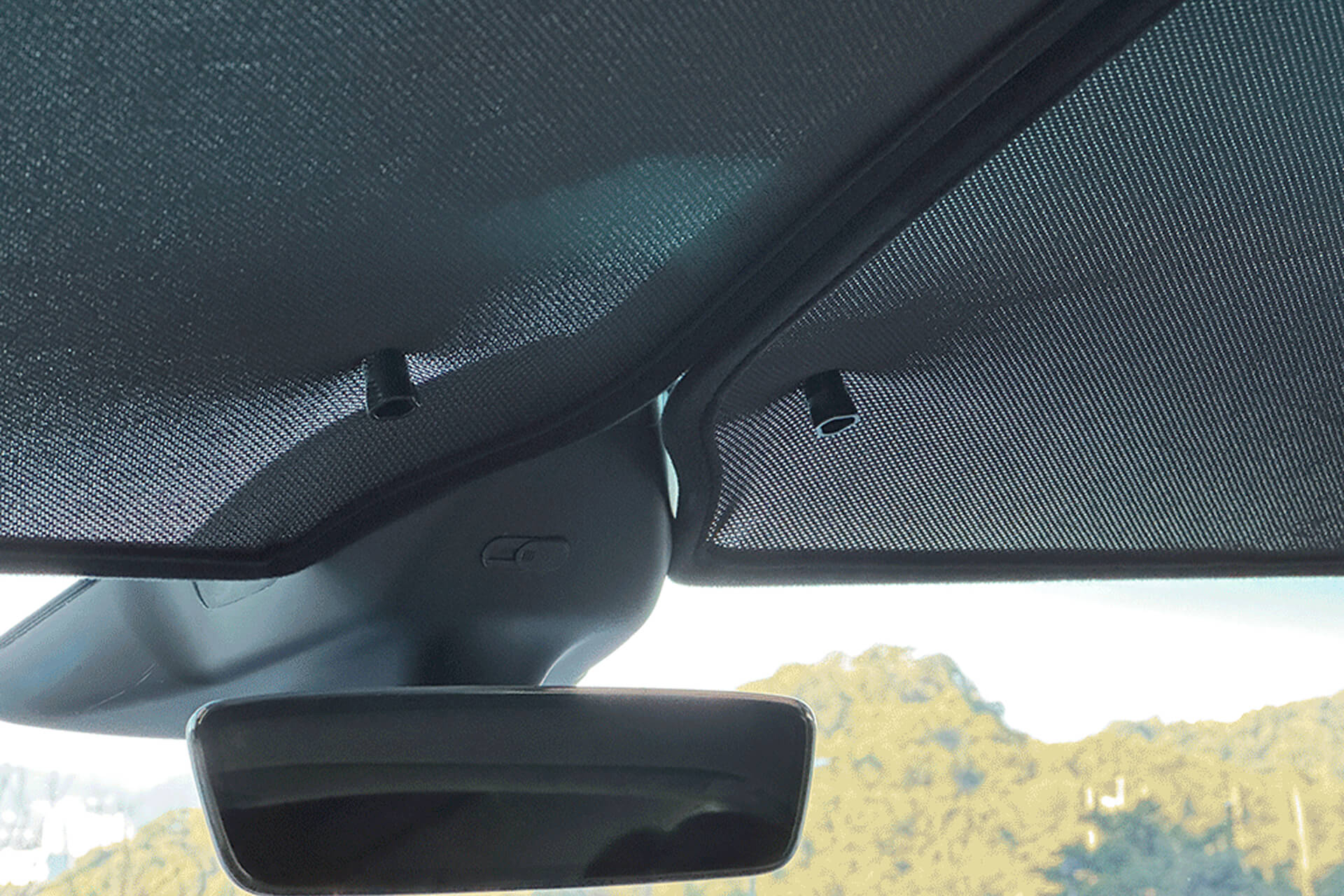 The car's interior showcases JOWUA's Glass Roof Sunshade- Separate Design (Model X), partially covered by a mesh sunshade to block UV rays. Sunlight streams through the rear windows, highlighting a hilly landscape visible in the rear-view mirror.