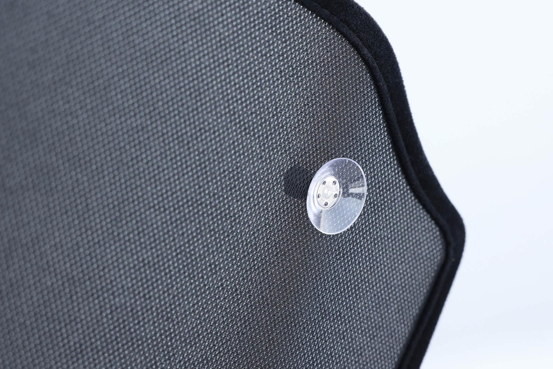 Close-up of a dark, textured JOWUA Glass Roof Sunshade-Mesh (Model X) with a transparent suction cup attached. The fabric curves like the Model X sunroof, casting a subtle shadow, with an out-of-focus background highlighting the material and suction cup.