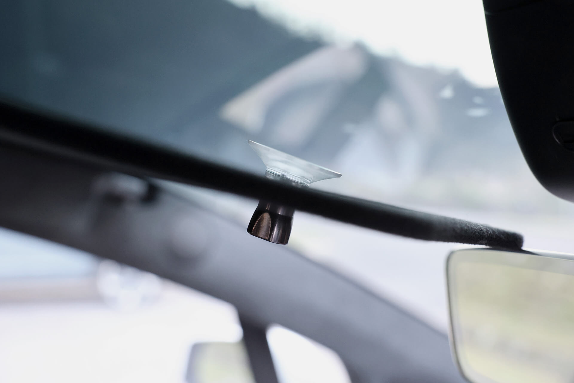 A close-up of a car's interior highlights the JOWUA Glass Roof Sunshade-Mesh (Model X) attached to the rearview mirror, providing UV protection. The blurred car interior emphasizes this practical accessory hanging with care from the mirror.