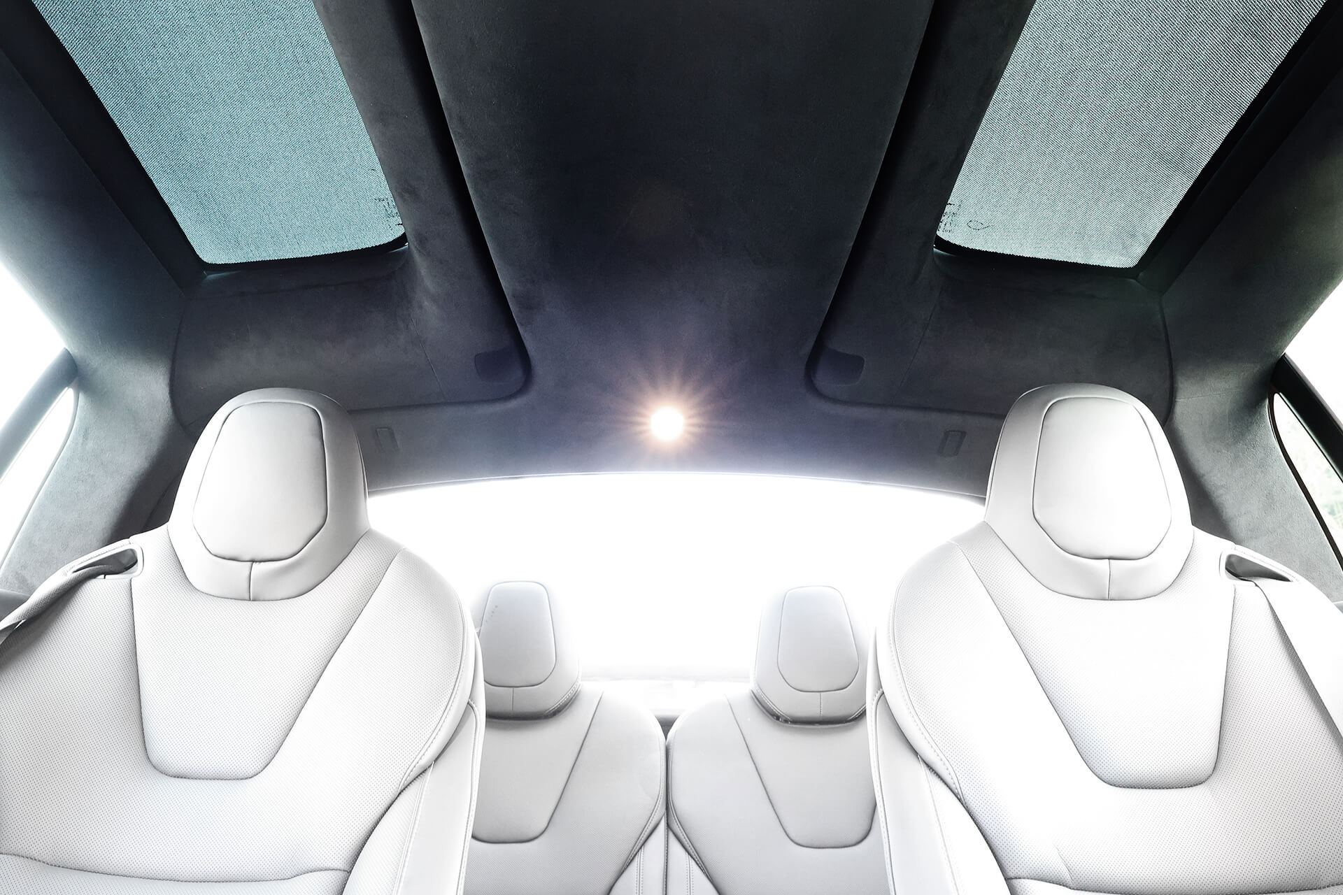 Interior of a futuristic car with sleek, white leather seats and minimalist design, featuring JOWUA's Glass Roof Sunshade-Mesh for Model X. The ceiling has panoramic UV-protective glass panels, and a central light adds an airy, modern touch.