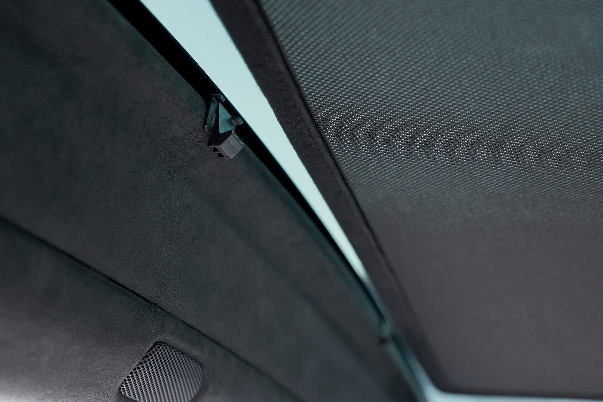 A close-up of the JOWUA Glass Roof Sunshade- Separate Design (Model X) features a partially closed mesh cover, highlighting its sleek design. The interior lining and small speaker or vent add a modern touch, efficiently blocking UV rays for enhanced automotive ambiance.