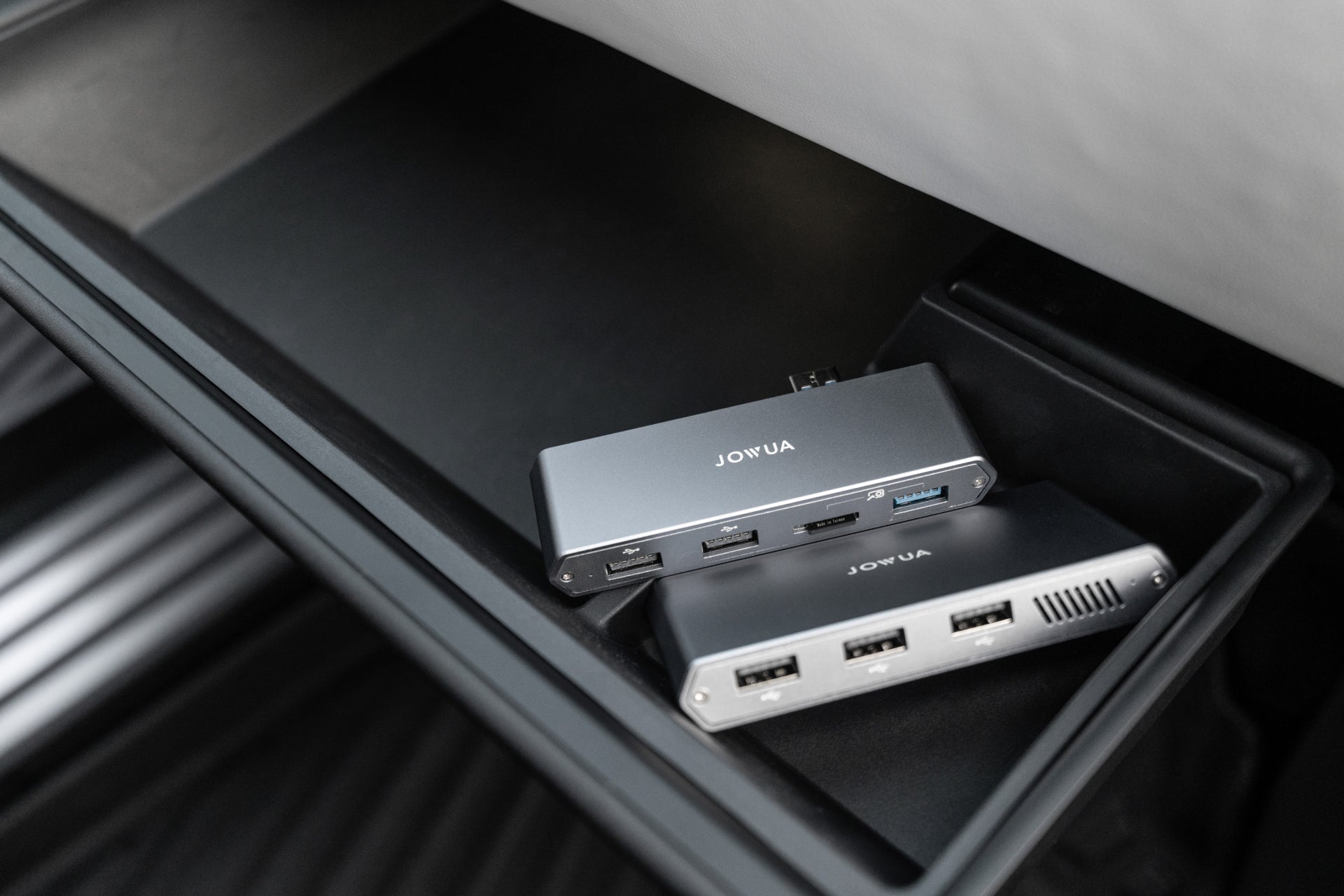 Inside the Tesla glovebox, two sleek black devices labeled "JOWUA" rest snugly. Each is a Dual-Function Storage HUB featuring multiple USB ports and a MicroSD reader, optimized for HW4.0.