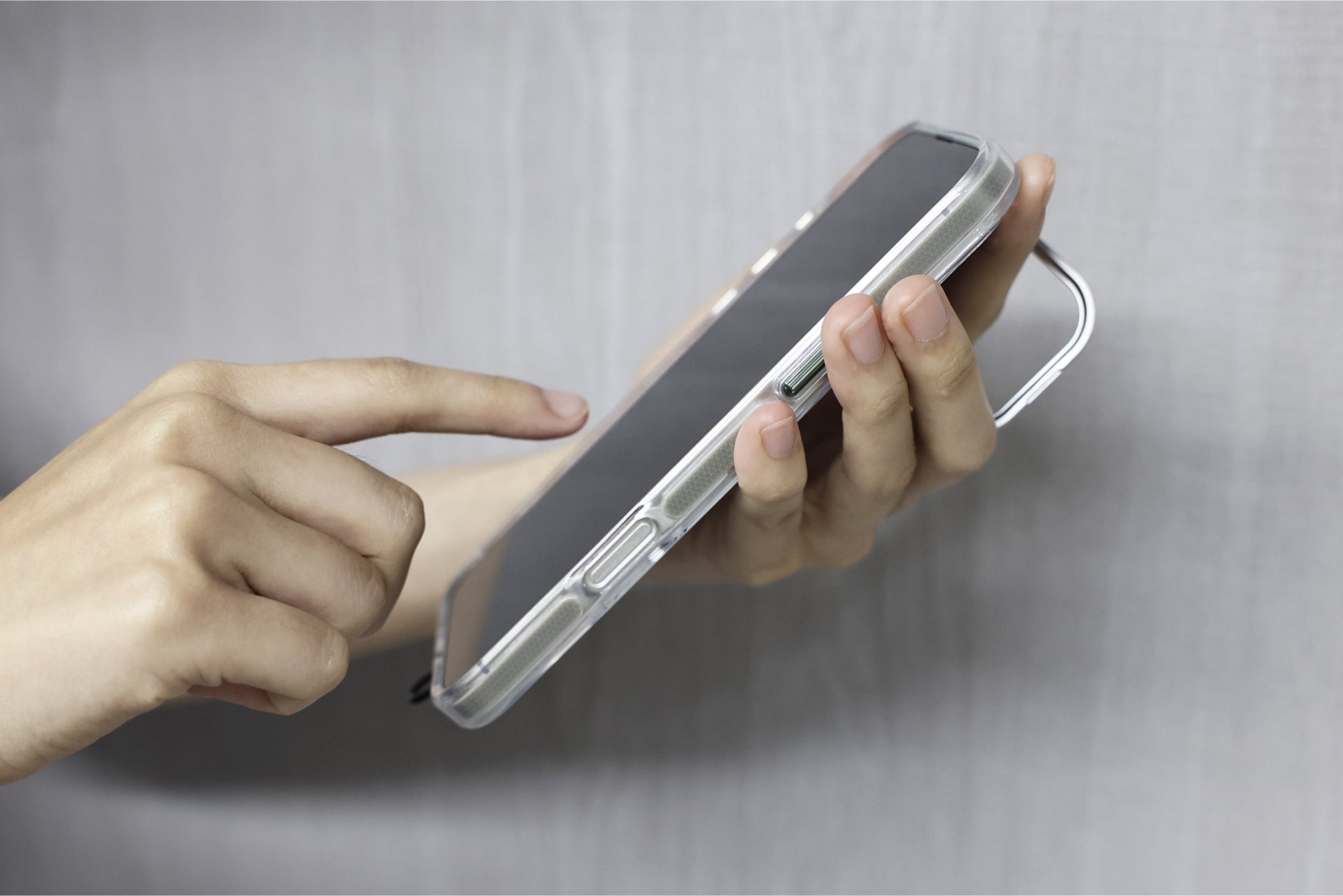 A person holding a JOWUA iPhone Case for Tesla Car Mount with MagSafe + Phone Tether Tab Set (iPhone 16 Series) in one hand and tapping the screen with the other against a plain background.