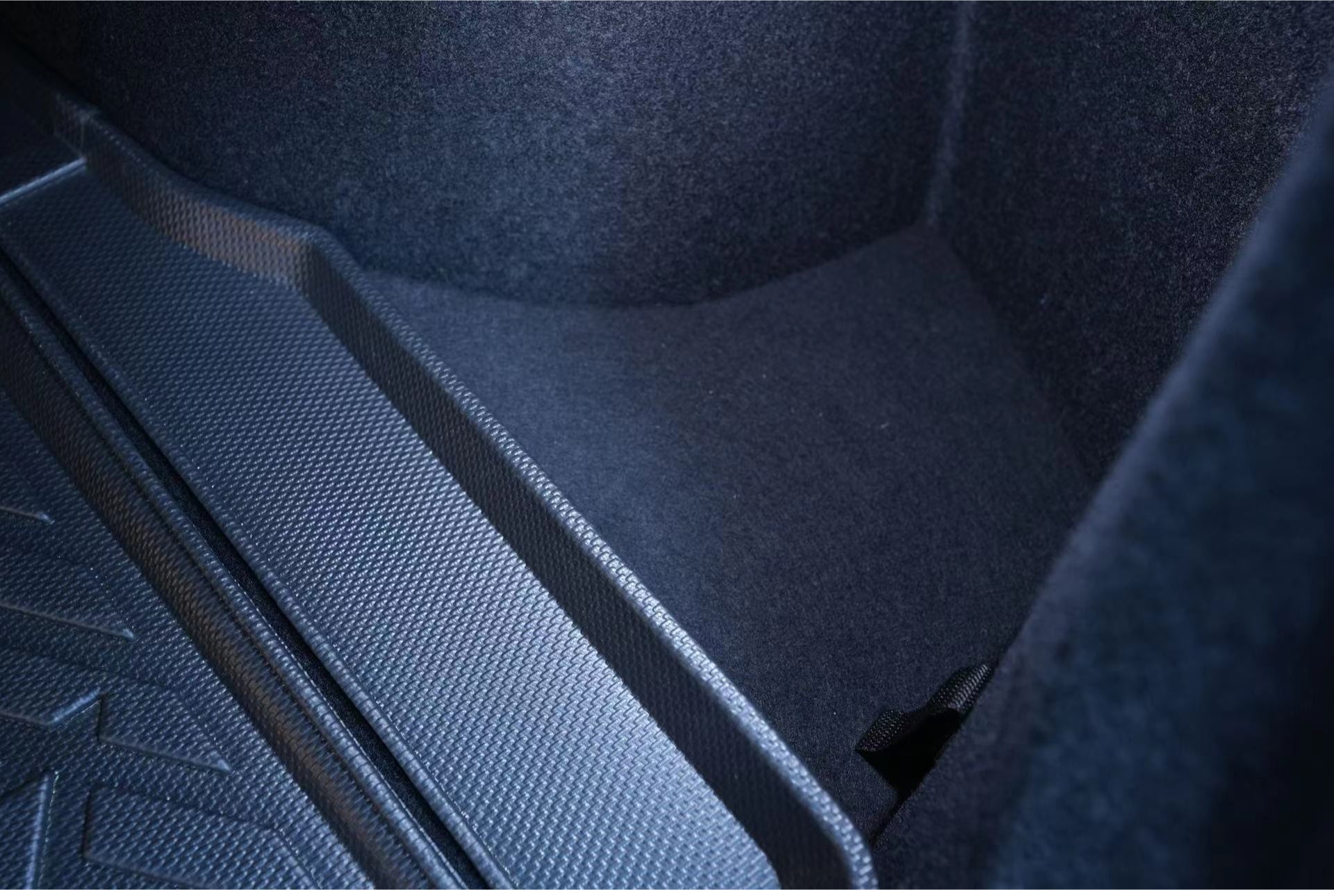 Close-up of a car trunk interior showcasing the JOWUA Model 3 All Weather Trunk Combo for the reengineered Model 3 Highland, 2024+. The textured black mats and fabric lining are illuminated, emphasizing the contours and durable, waterproof TPE material of the trunk space.