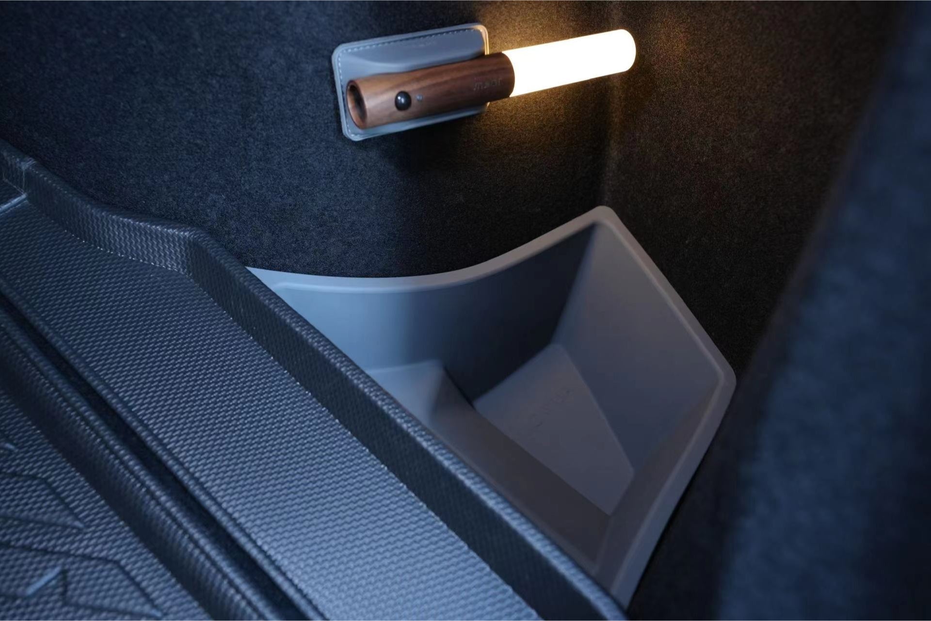 The JOWUA Model 3 All Weather Trunk Combo (Reengineered Model 3 Highland, 2024+) features a small, bright flashlight attached to the side within its interior utility compartment. The space is lined with textured rubber matting and includes a light gray plastic bin-like section, reminiscent of high-quality trunk liners.