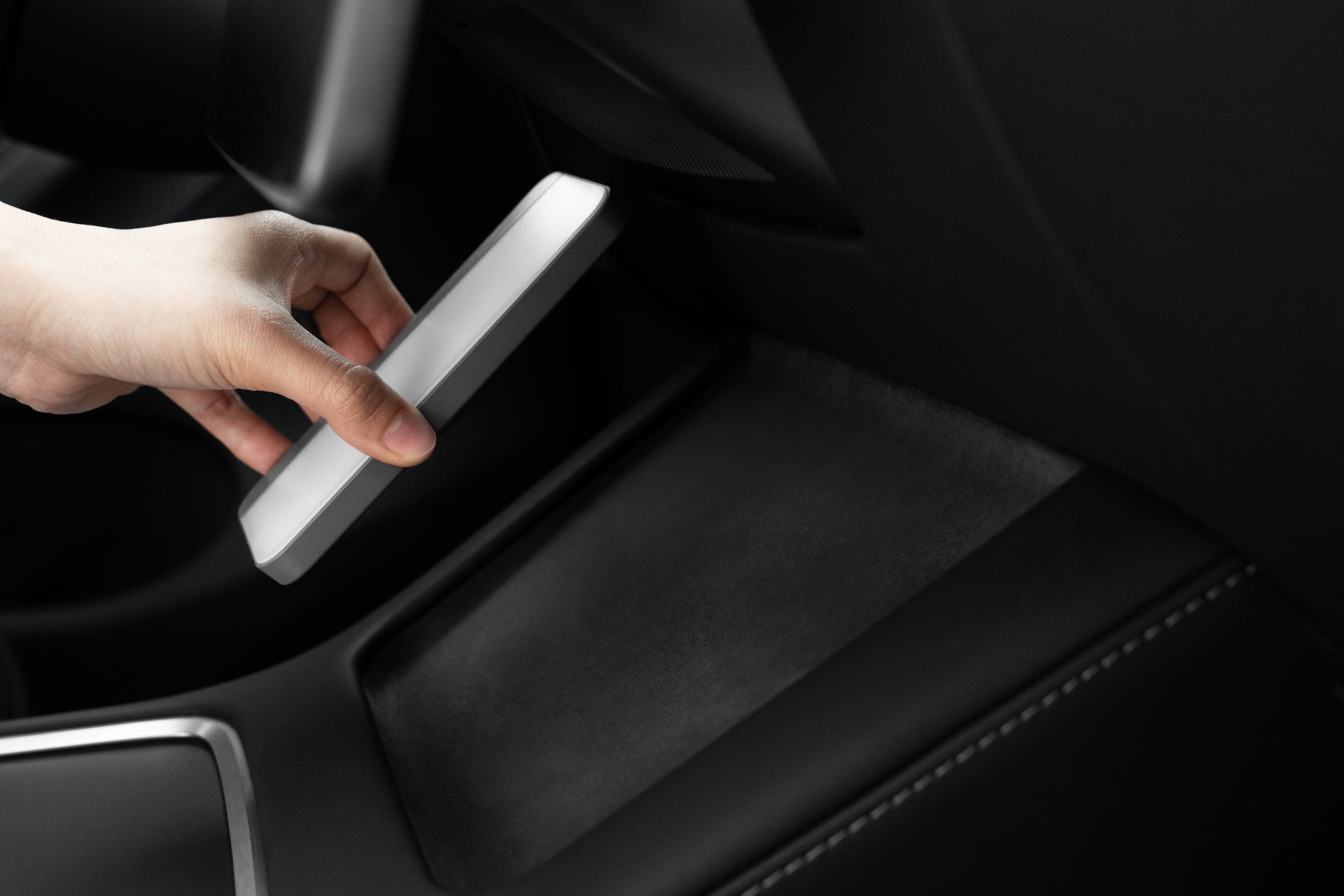 A hand places the JOWUA LED Center Console Combo, designed specifically for the Tesla Reengineered Model 3 Highland (2024+), into the car's interior organizer. The vehicle boasts sleek black upholstery and modern design elements enriched with premium silicone materials for an elegant touch.