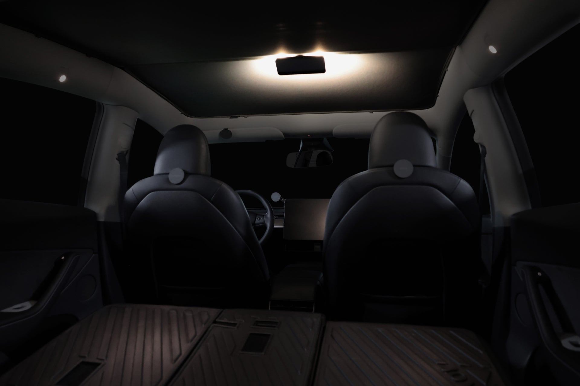 The interior of the Tesla Reengineered Model 3 Highland (2024+) by JOWUA showcases two front seats, a center console equipped with the LED Center Console Combo for an innovative organizer solution, and a stylish dashboard. The dim lighting emphasizes the sleek, modern design that includes what seems to be a foldable rear seat. This dark and spacious vehicle features elegant accents crafted from premium silicone for added refinement.